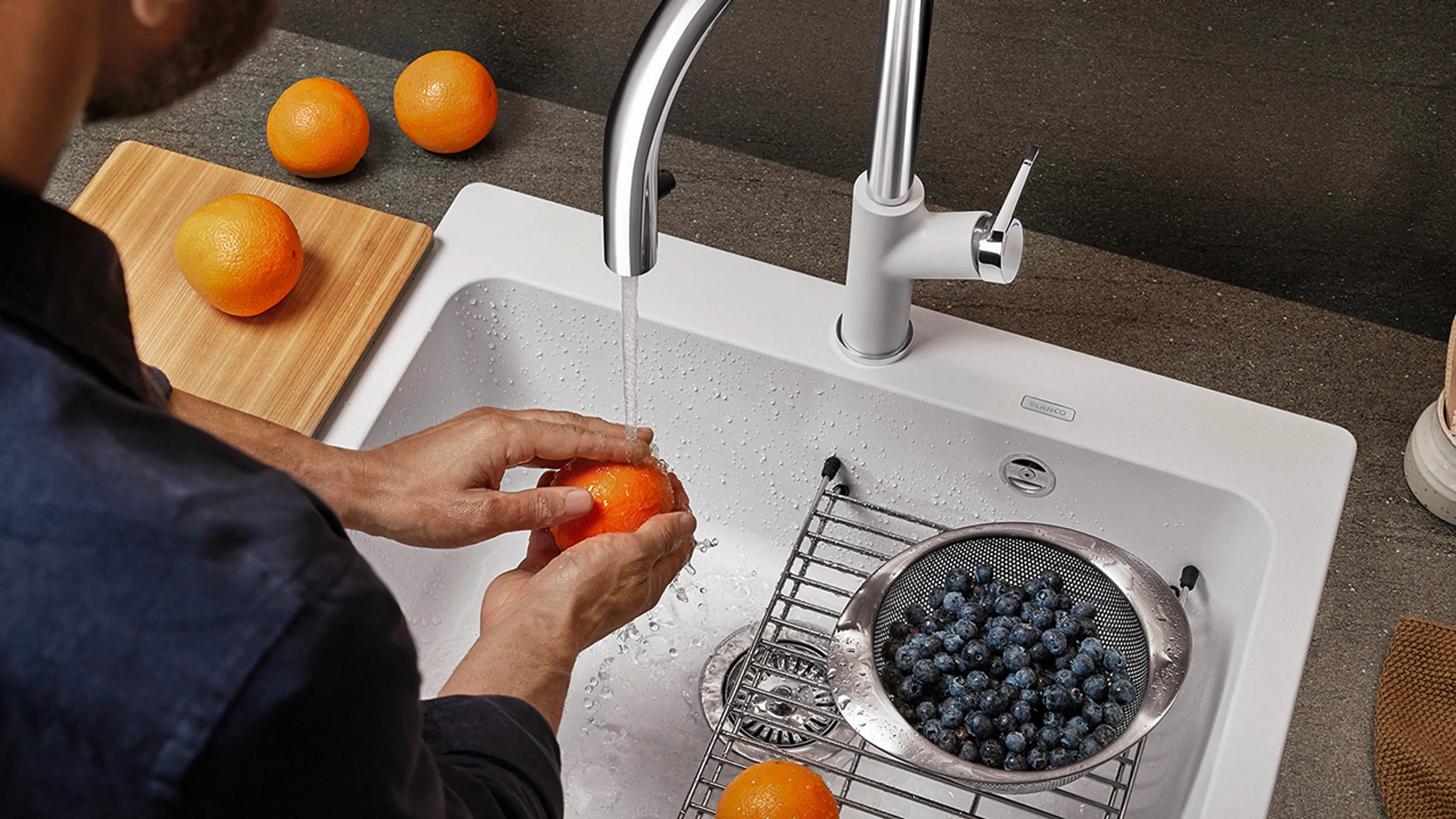 Mann som vasker appelsiner og blåbære i kjøkkenvask med smarte løsninger.