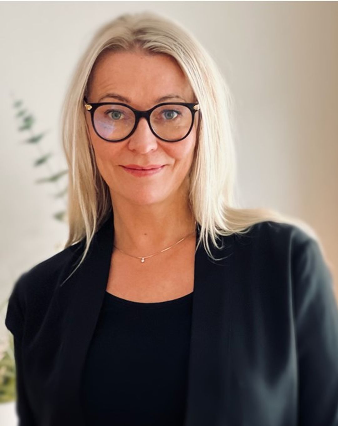 Rektor i Sonans Fredrikstad, Tine Spillberg, smiler iført svarte briller og blazer mot lys bakgrunn.