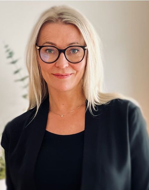 Rektor i Sonans Tønsberg, Tine Spillberg, smiler iført svarte briller og blazer mot lys bakgrunn.