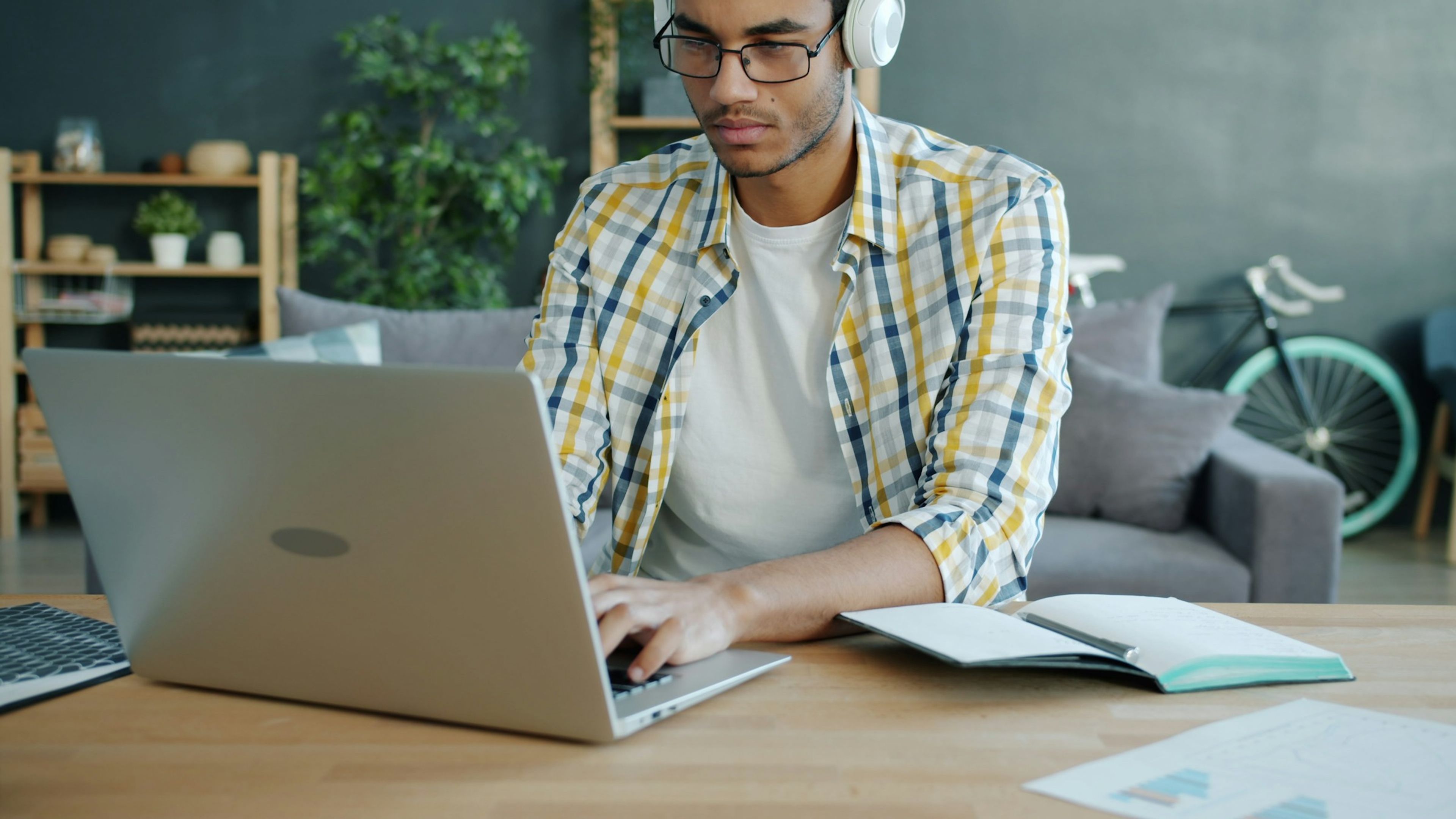 Person studerer hjemme ved hjelp av laptop, notater og hodetelefoner.