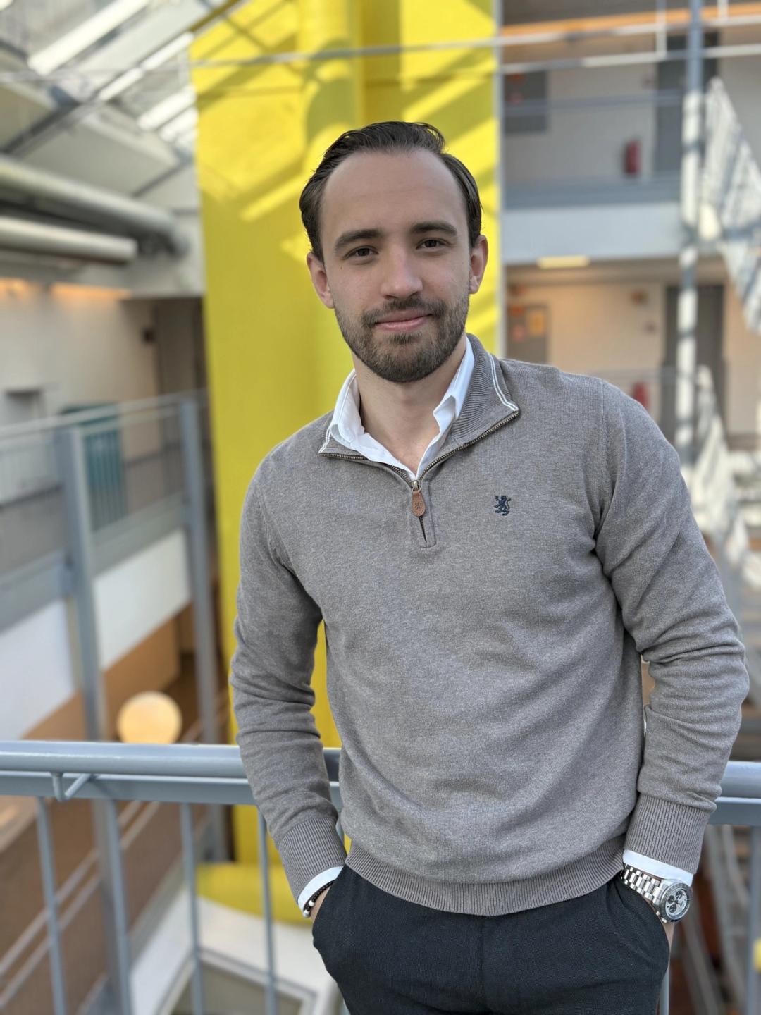 Avdelingsleder ved Sonans Oslo,  Emil Buarøy, smiler i et lyst atrium med gule detaljer i bakgrunnen.