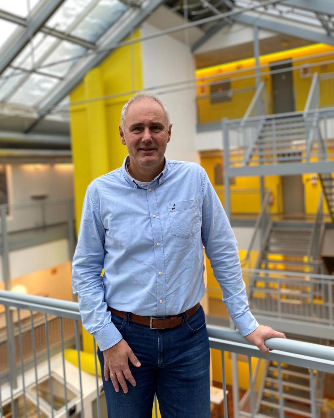 Rektor i Sonans Tromsø, Terje Aas, smiler i et lyst atrium med gule detaljer i bakgrunnen.