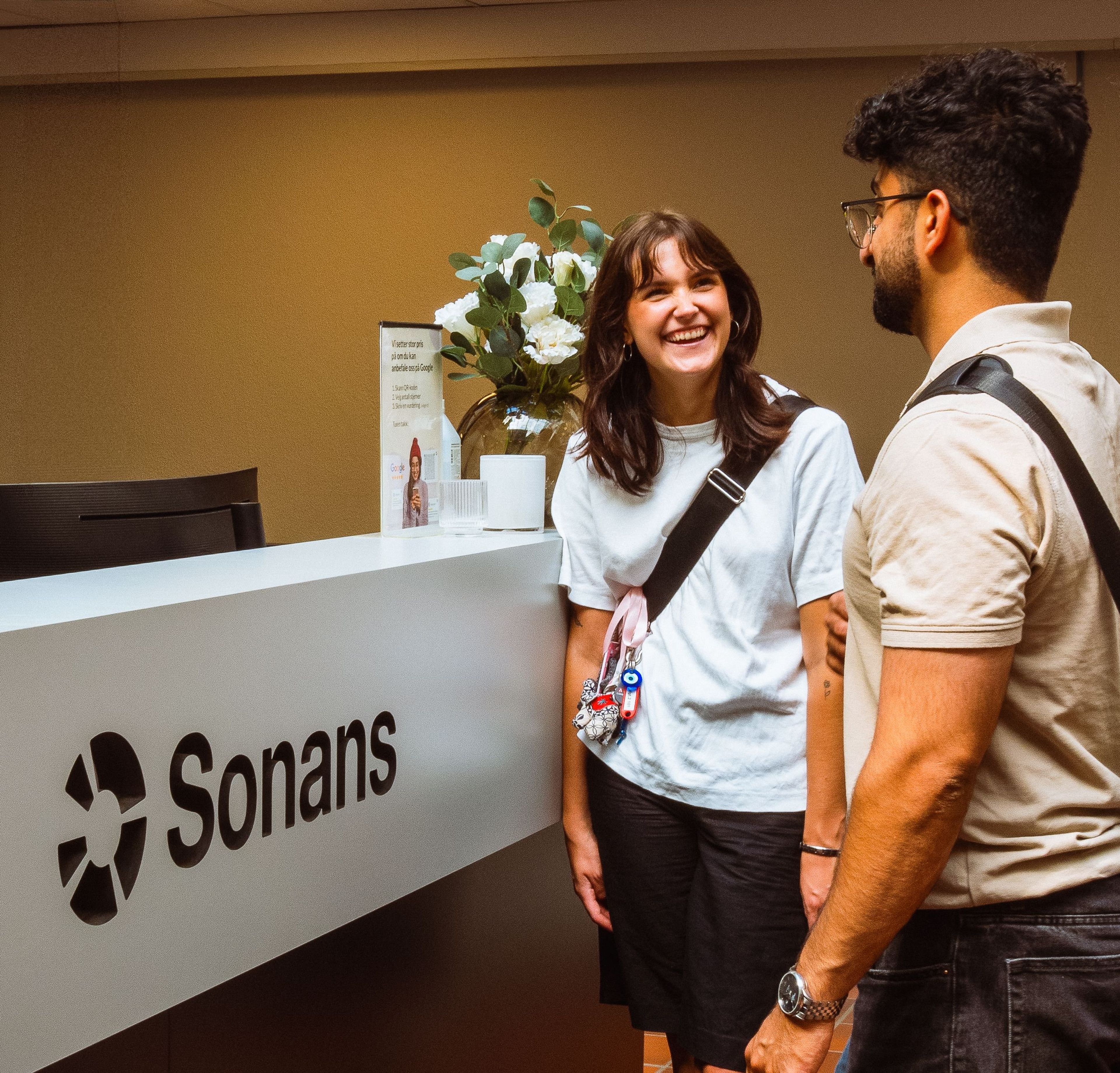 Smilende privatist står ved Sonans resepsjon med blomster i bakgrunnen.