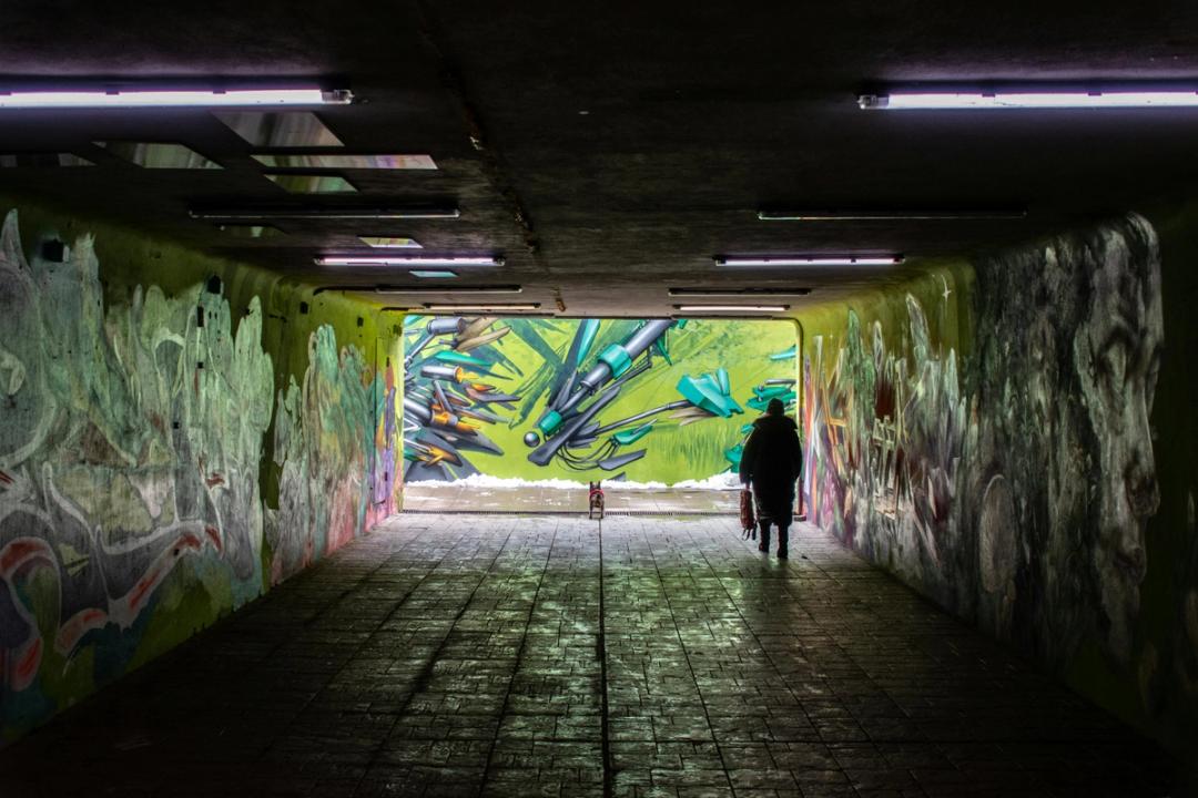 Bildet viser et en person som går tur med en liten hund, gjennom en undergang med grafitti på veggene