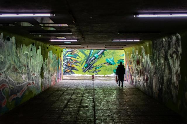 Bildet viser et en person som går tur med en liten hund, gjennom en undergang med grafitti på veggene