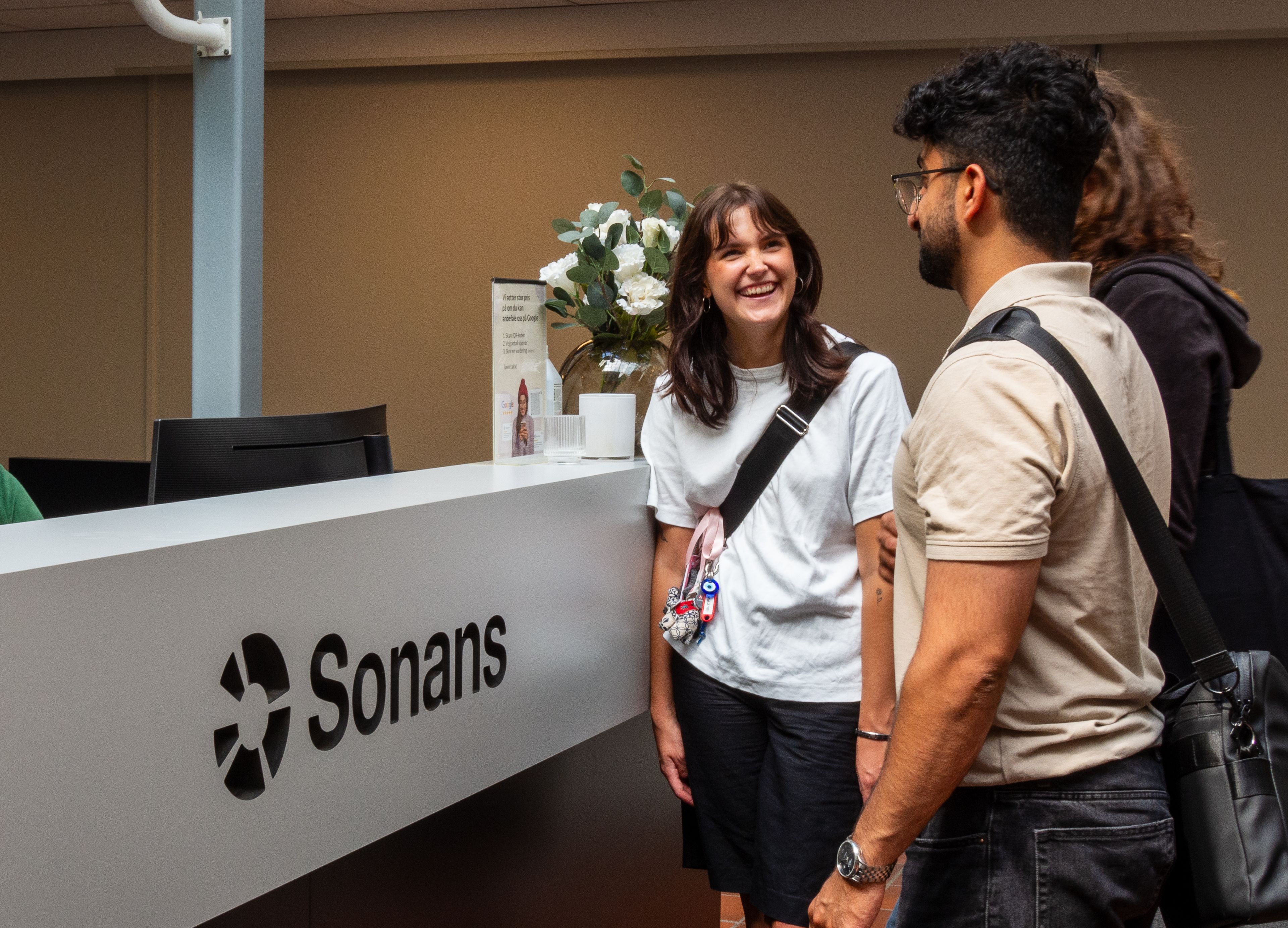 Smilende studenter ved resepsjonen på Sonans, engasjert i en samtale.