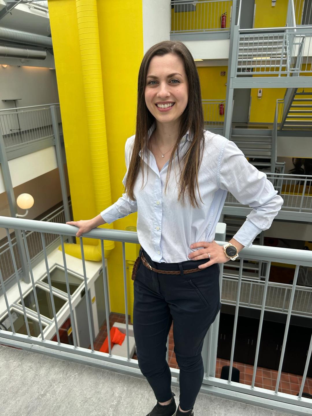Rektor i Sonans Trondheim, Elina Jacobsen, smiler i et lyst atrium med gule detaljer i bakgrunnen.
