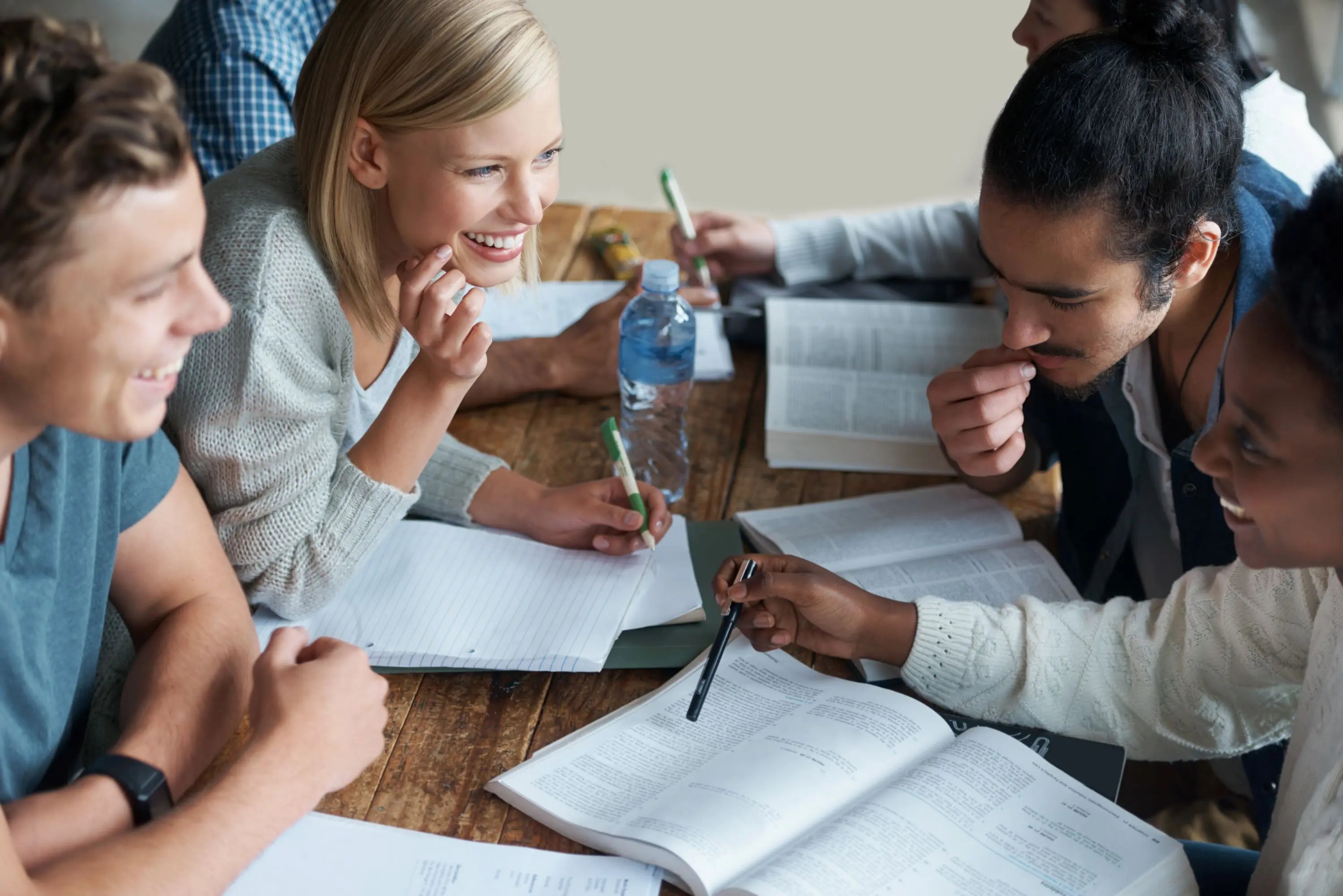 Studenter jobber sammen rundt et bord med bøker og notater, mens de smiler og diskuterer.
