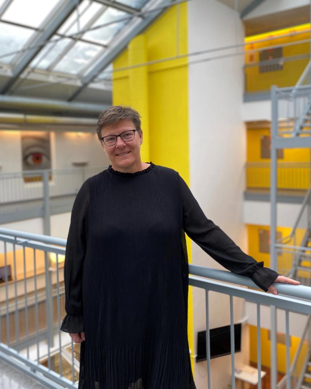 Rektor i Sonans Bergen, Mette Knutsen, smiler i et lyst atrium med gule detaljer i bakgrunnen.