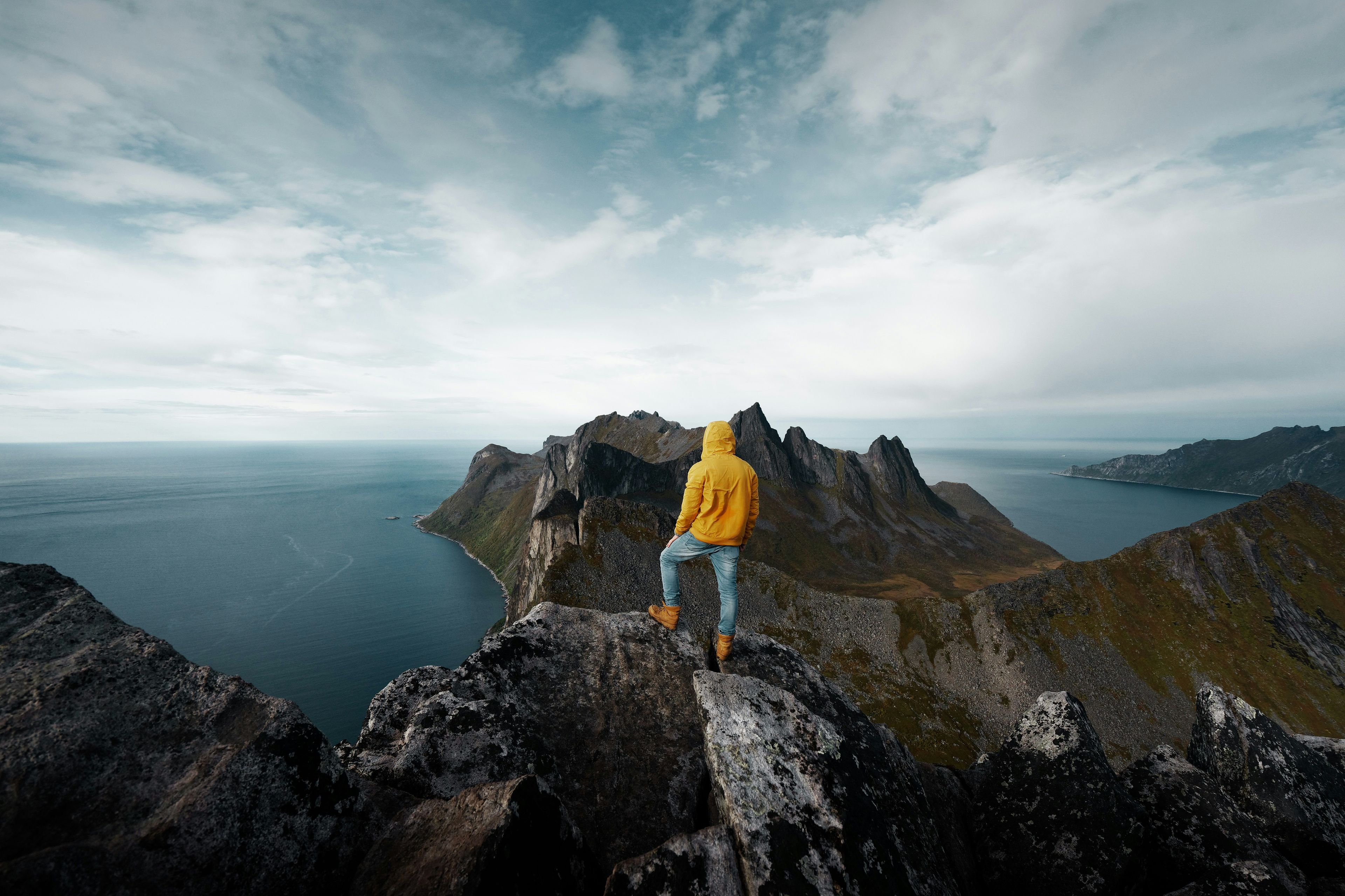 Person i gul jakke står på en fjelltopp med utsikt over norsk kystlandskap - symboliserer nye muligheter og personlig vekst i Norge.