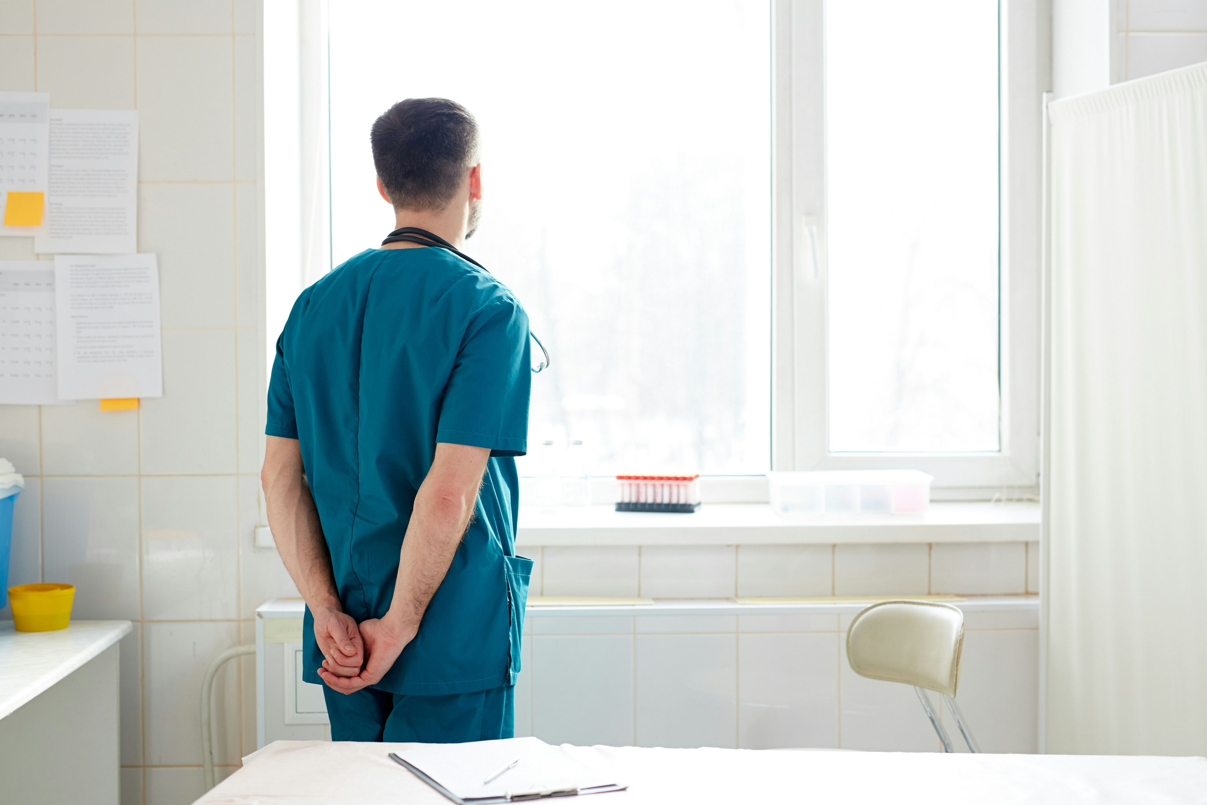 Helsearbeider i uniform ser ut av vinduet på klinikk.