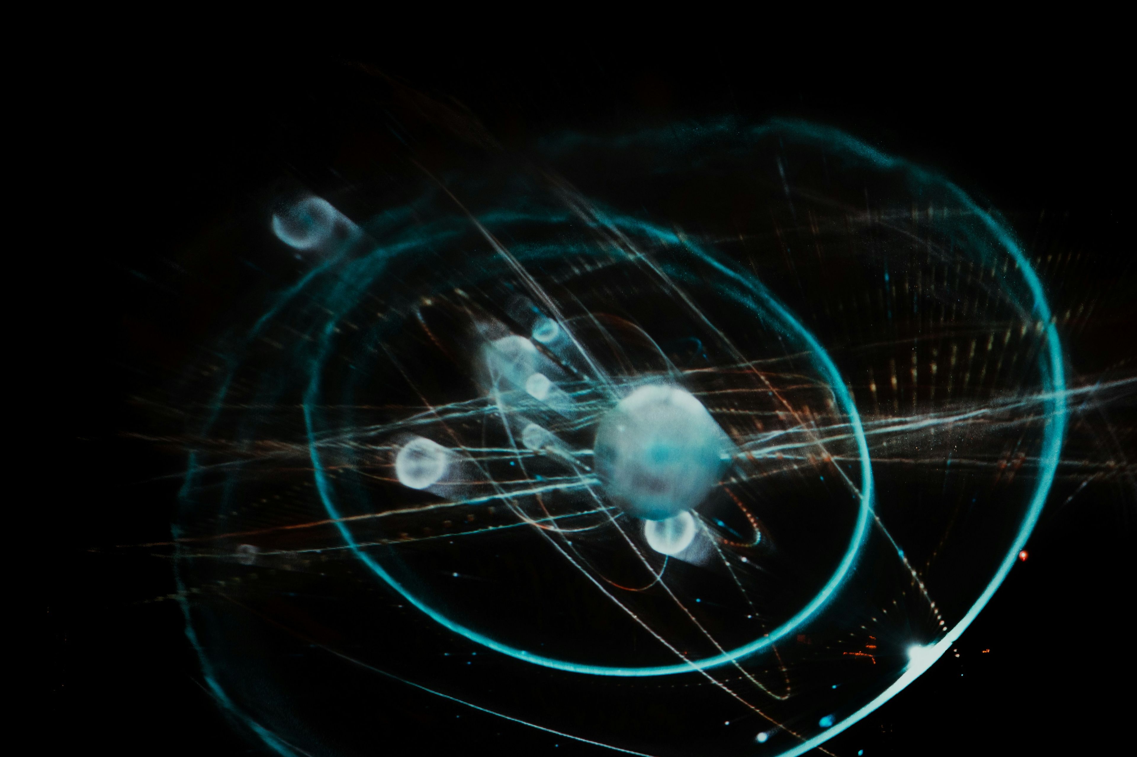 Modell av et atom, med en kjerne i midten og flere partikler som beveger seg i baner rundt den. Det er lysende linjer og spor som gir inntrykk av energi og bevegelse.