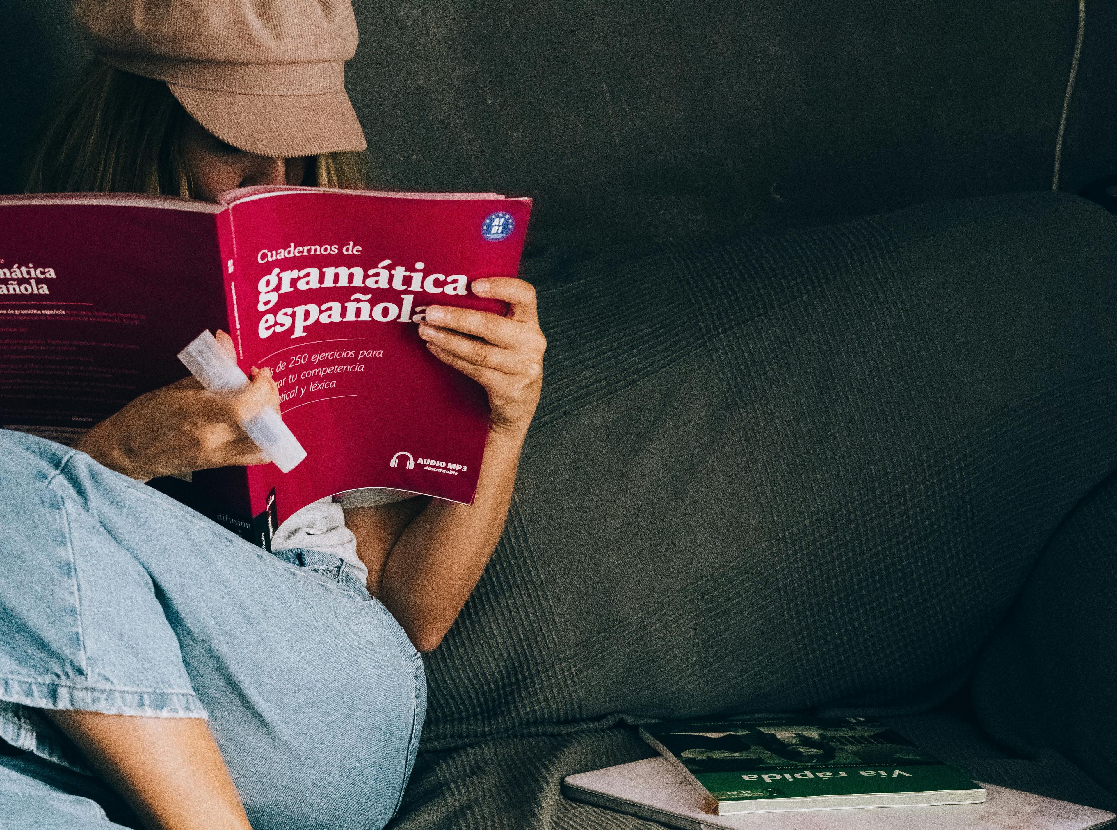 Student sitter i en grønn sofa og leser i en spansk grammatikkbok.