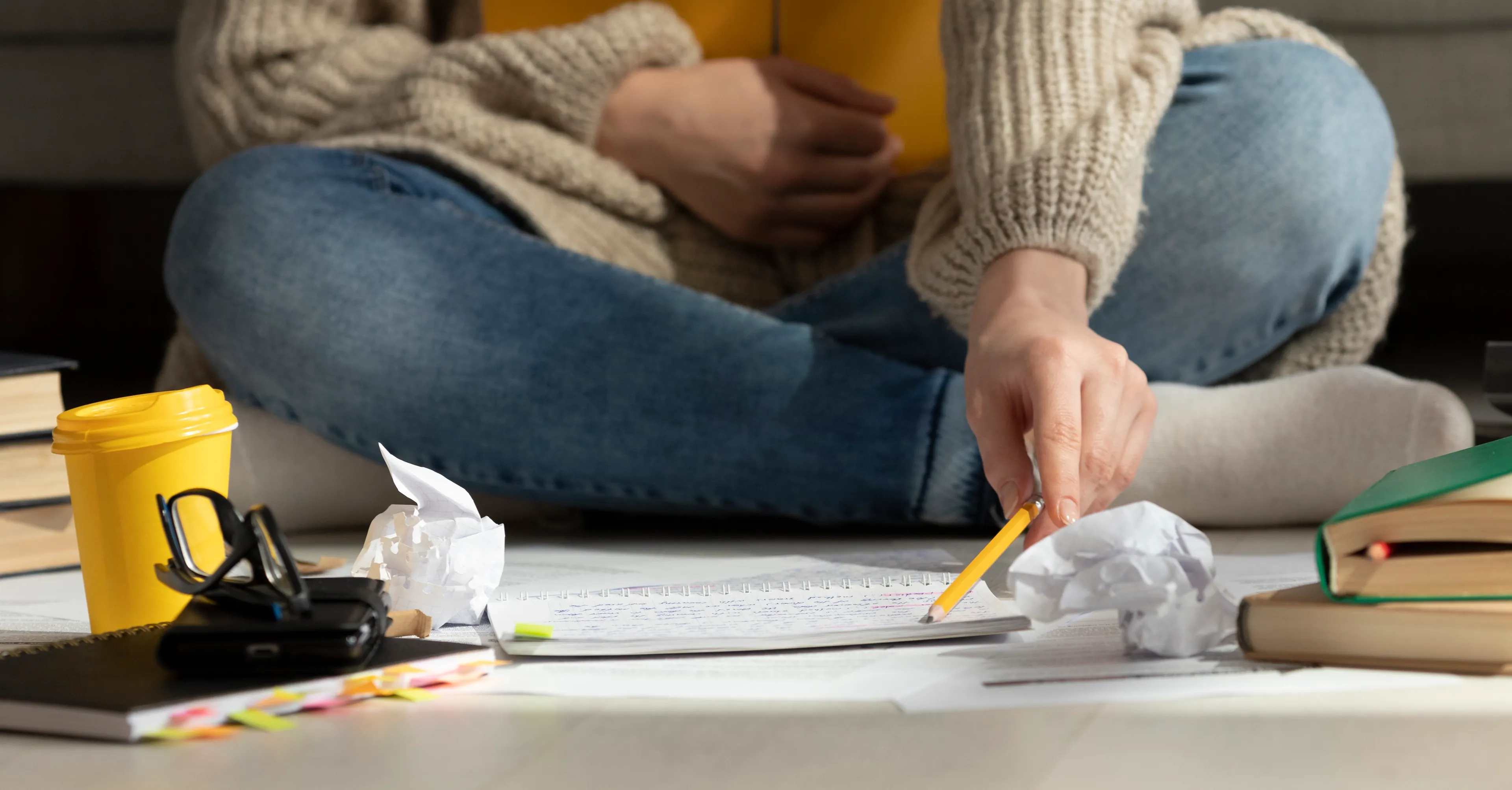 Student som sitter på gulvet, med bøker og notatblokk.