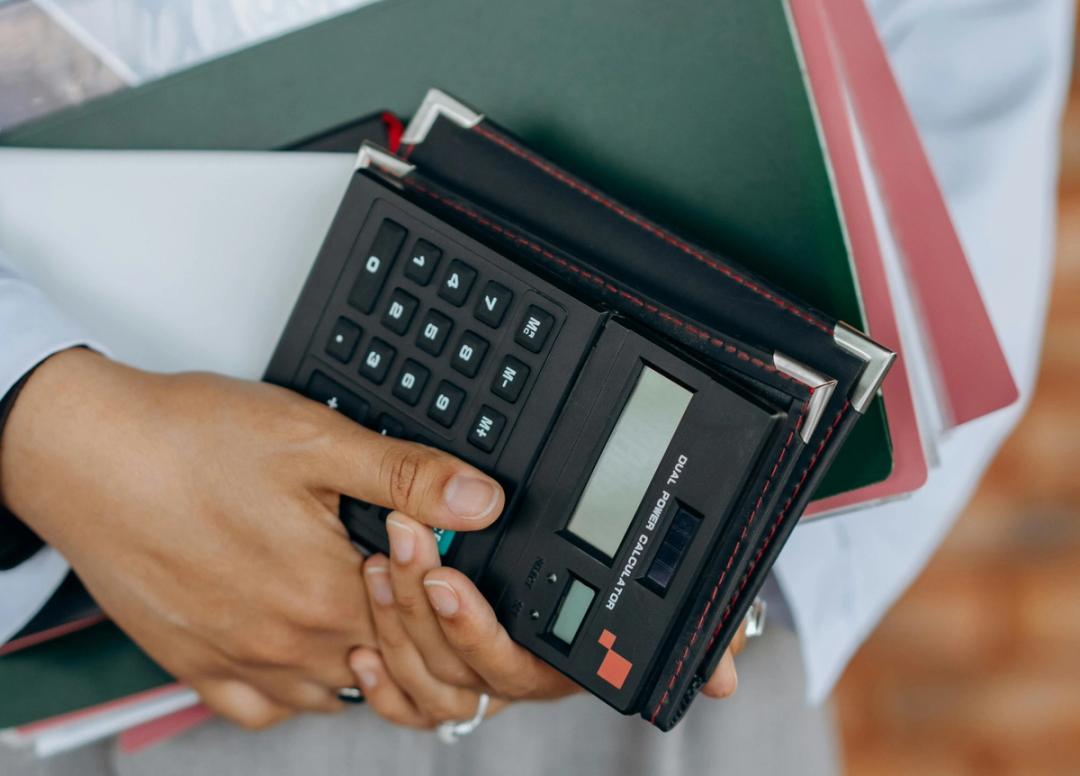En person holder en kalkulator og noen notatbøker.