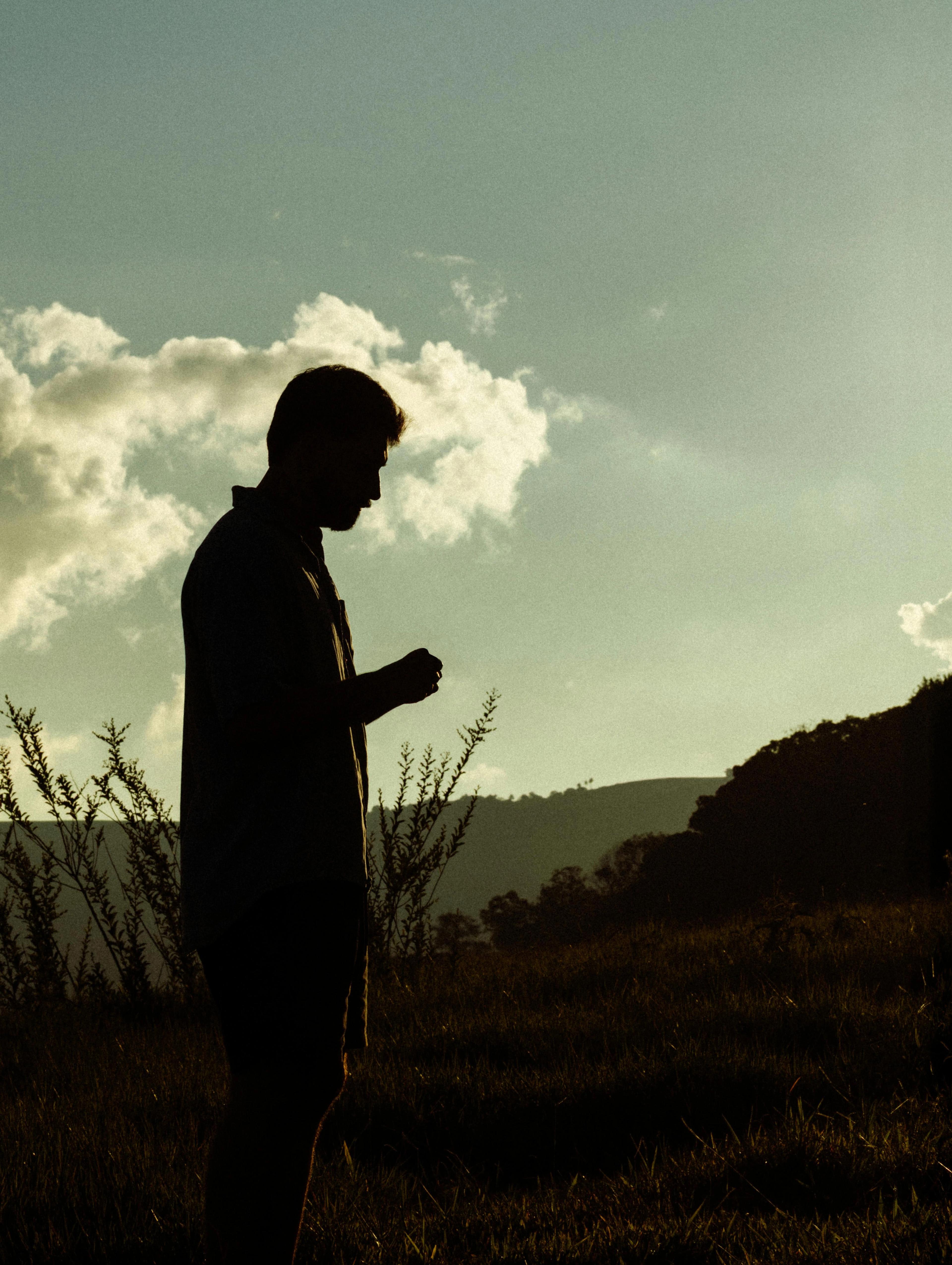 Silhouette av en mann i stille refleksjon, ute i naturen.