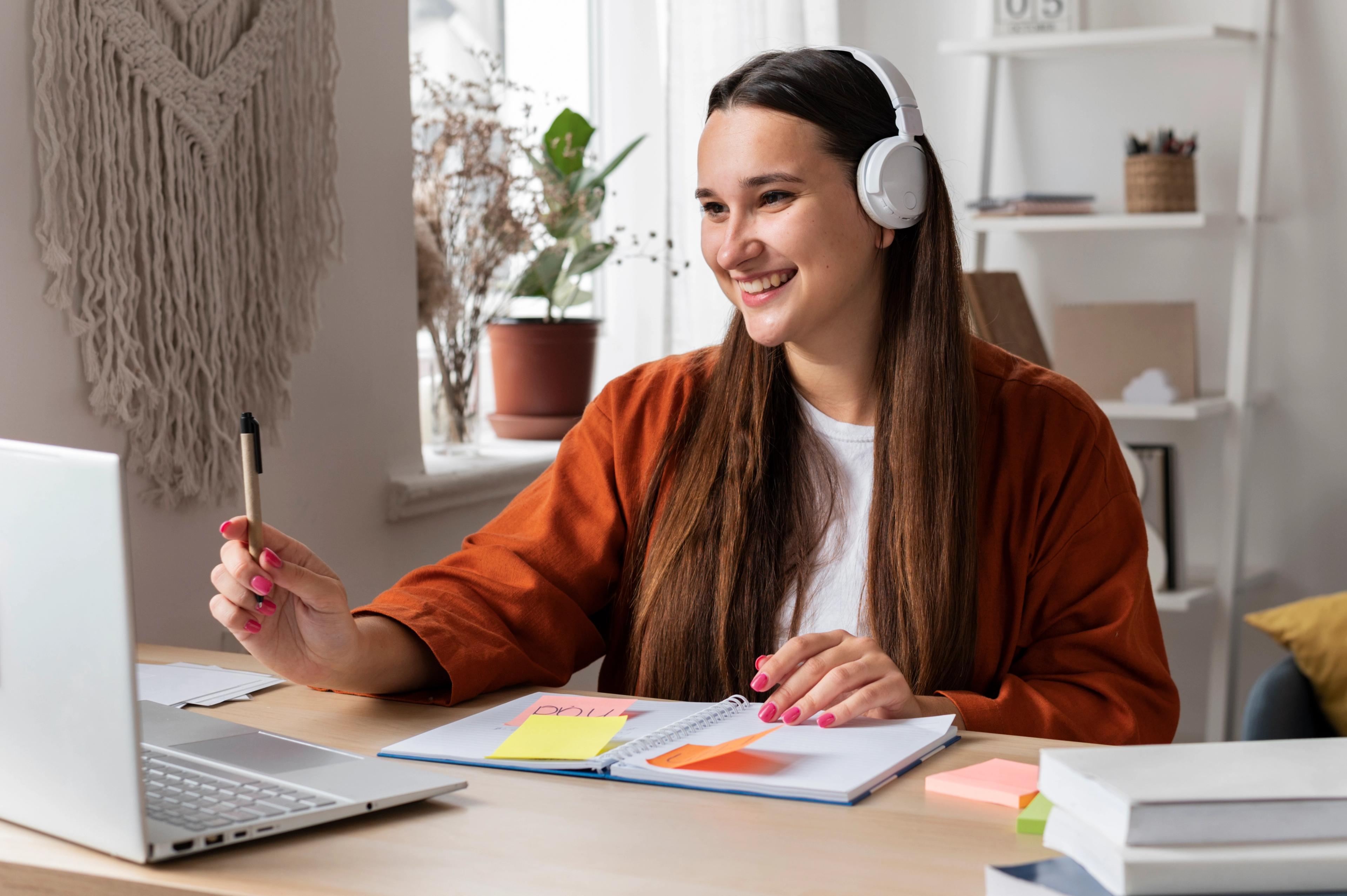 Smilende student med hodetelefoner i nettmøte med rådgiver - tar notater og får hjelp til fagvalg og poengberegning hjemmefra.