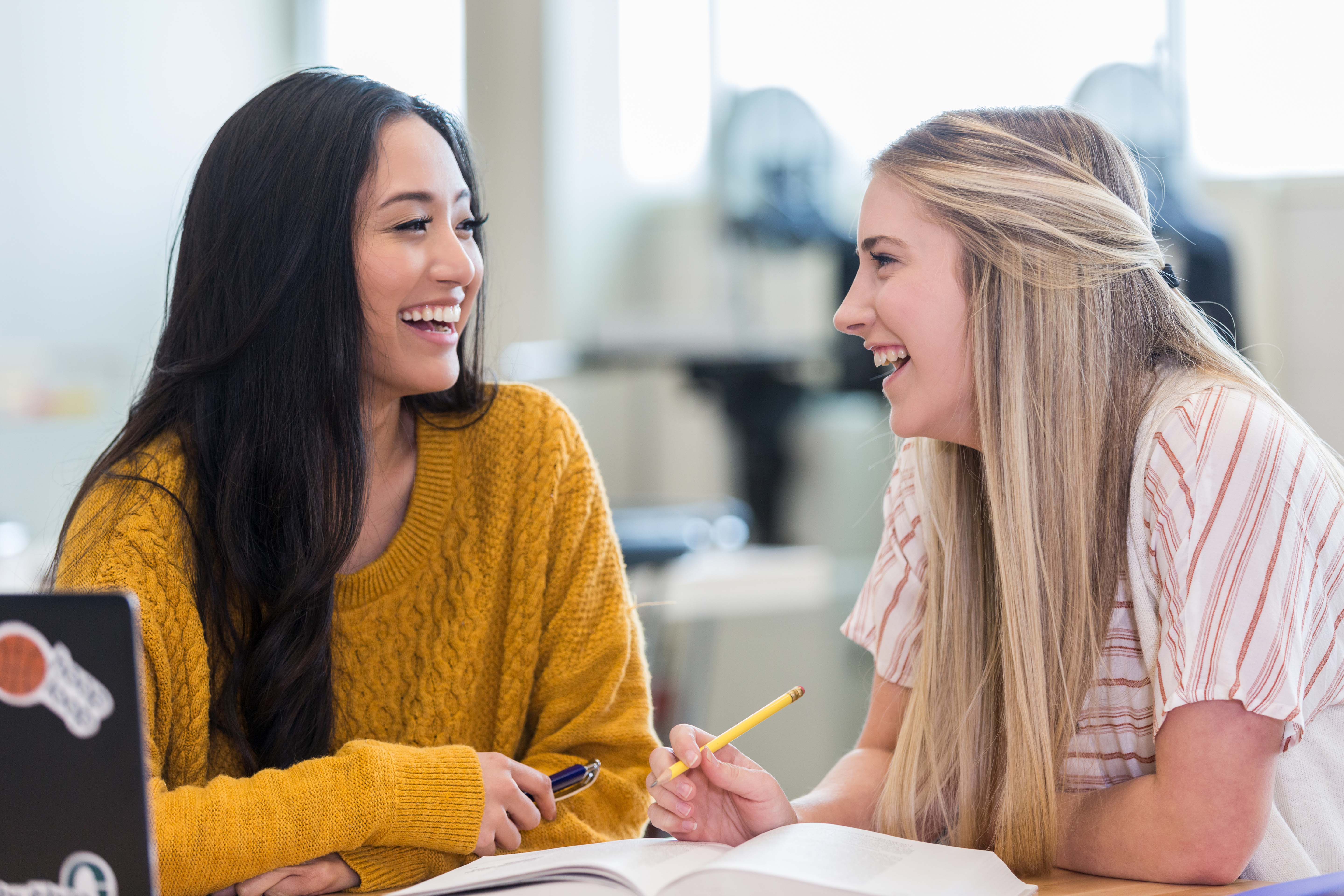 To Sonans studenter smiler og snakker sammen mens de jobber.