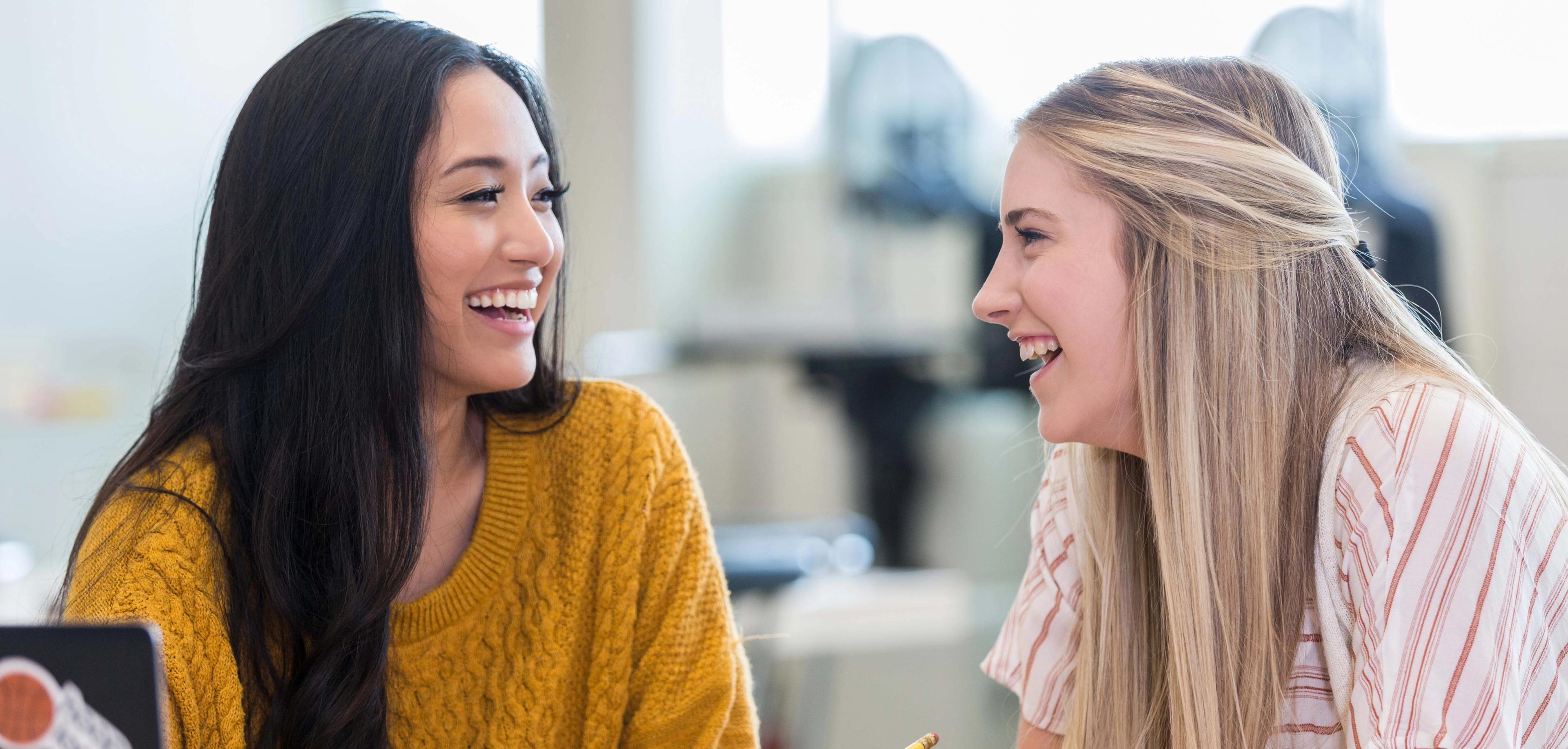 To Sonans studenter smiler og snakker sammen mens de jobber.