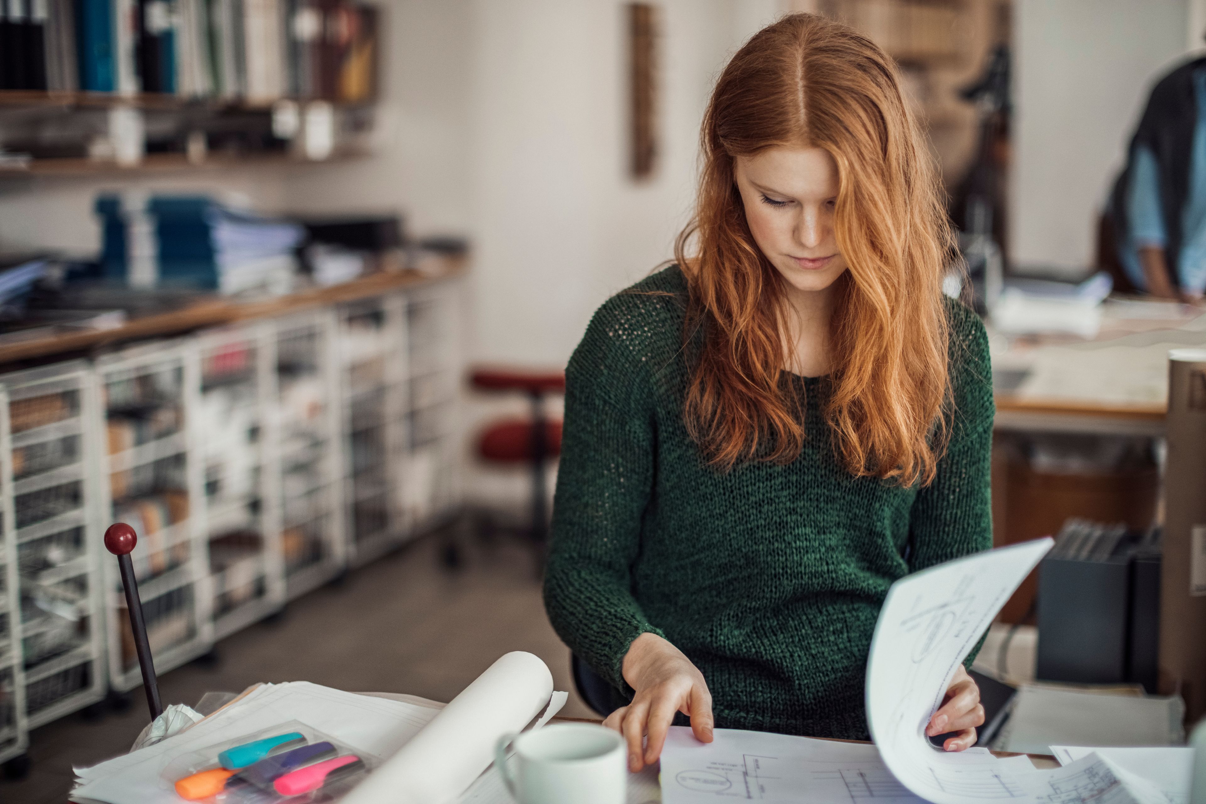 Student i grønn genser jobber med eksamensforberedelser, ser på notater ved et skrivebord.