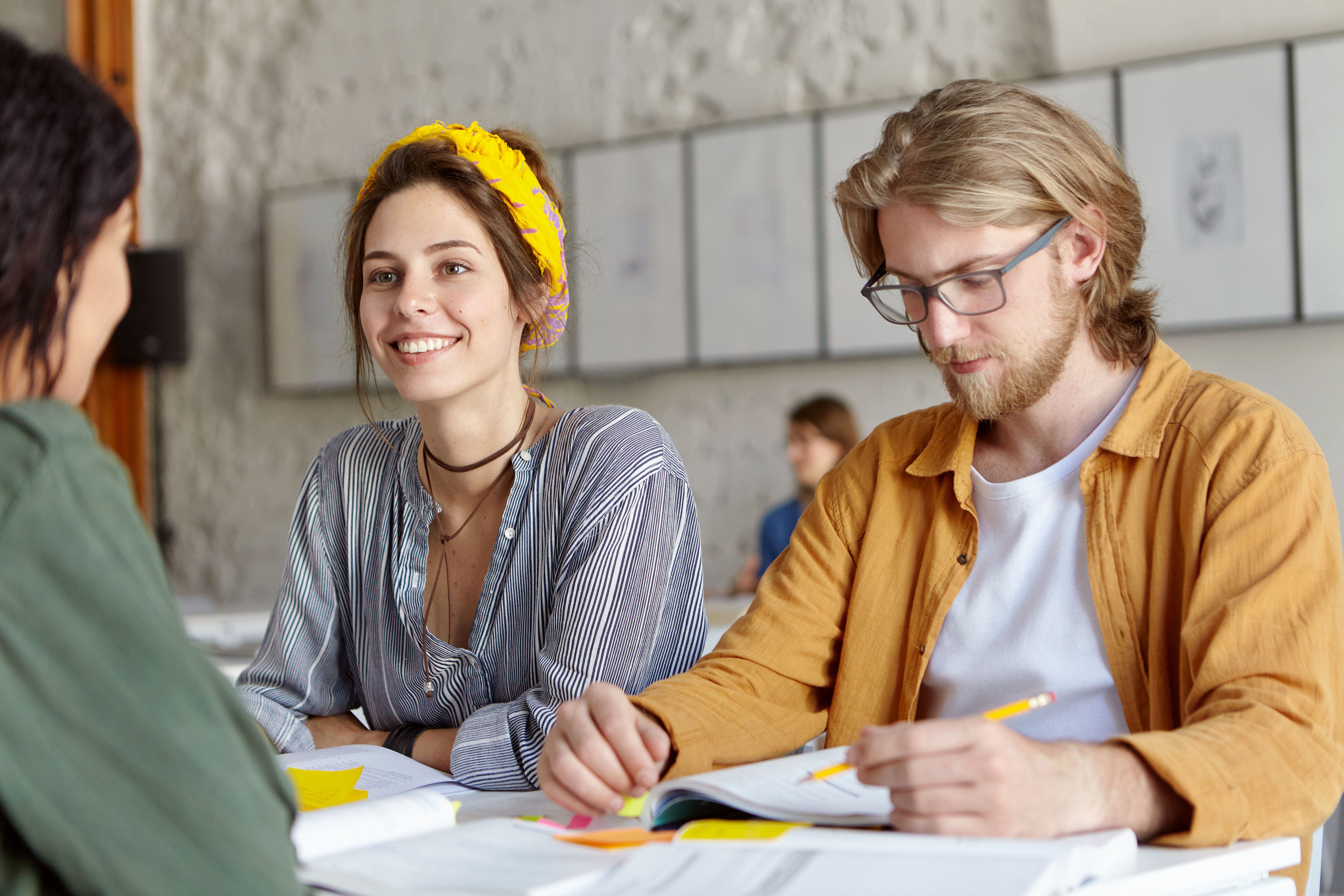 En gruppe studenter sitter sammen ved et bord og jobber med notater, mens de smiler og prater.