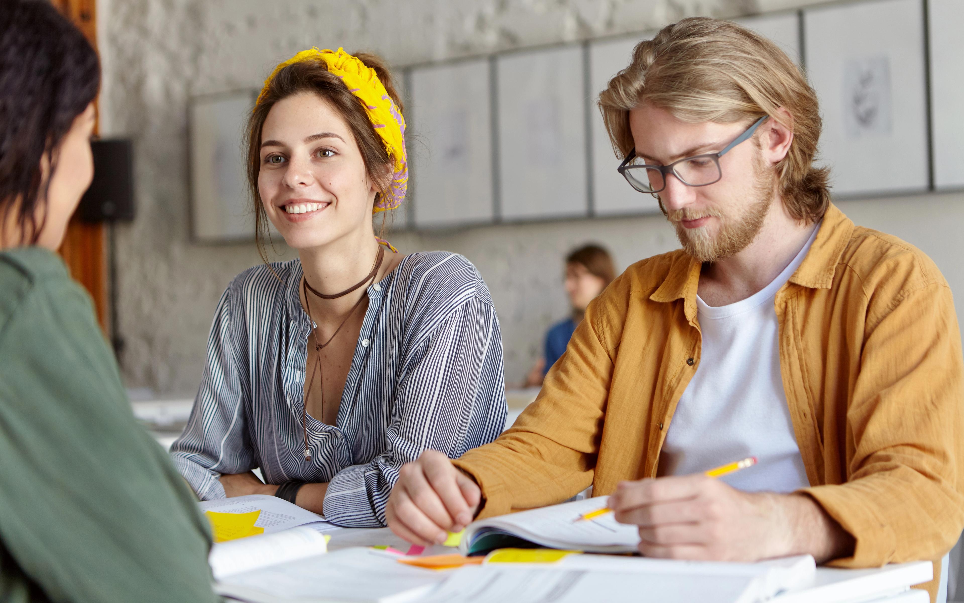 En gruppe studenter sitter sammen ved et bord og jobber med notater, mens de smiler og prater.