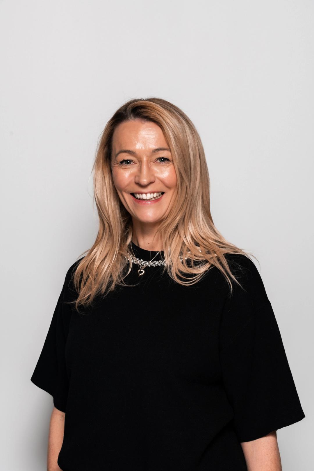 Avdelingsleder i Sonans Fredrikstad, Tine Spillberg, smiler mot lys bakgrunn.