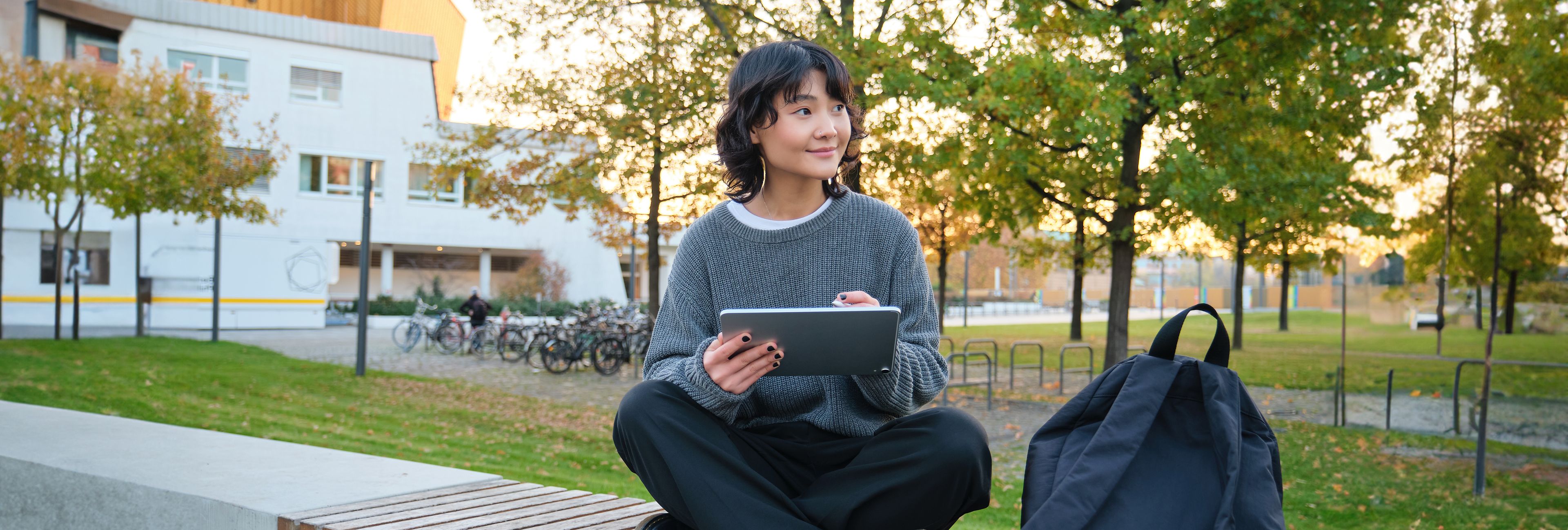 Kvinnelig student sitter ute på en benk og skriver på et nettbrett.