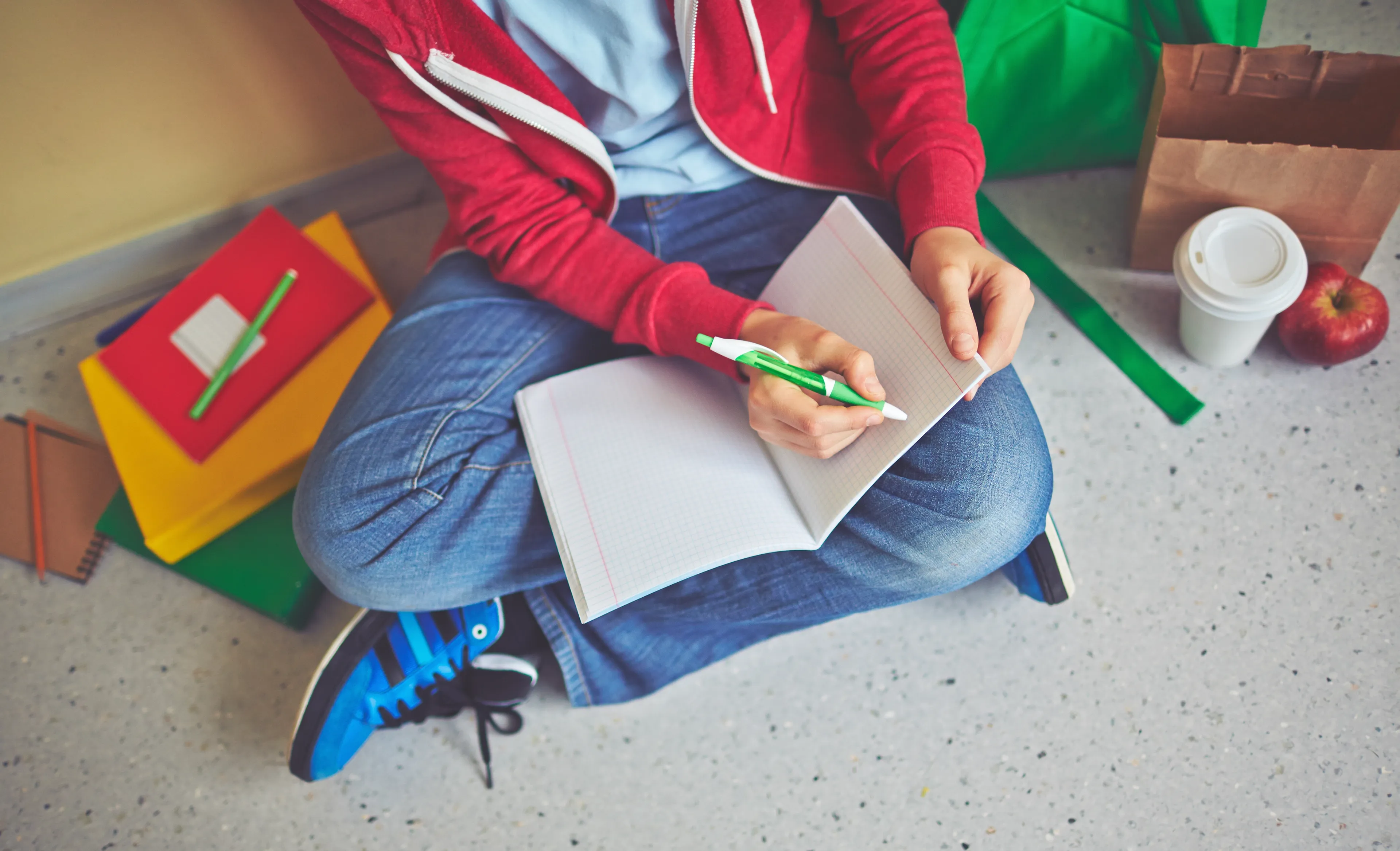 Student sitter på gulvet med kryssede ben og skriver i en notatbok.