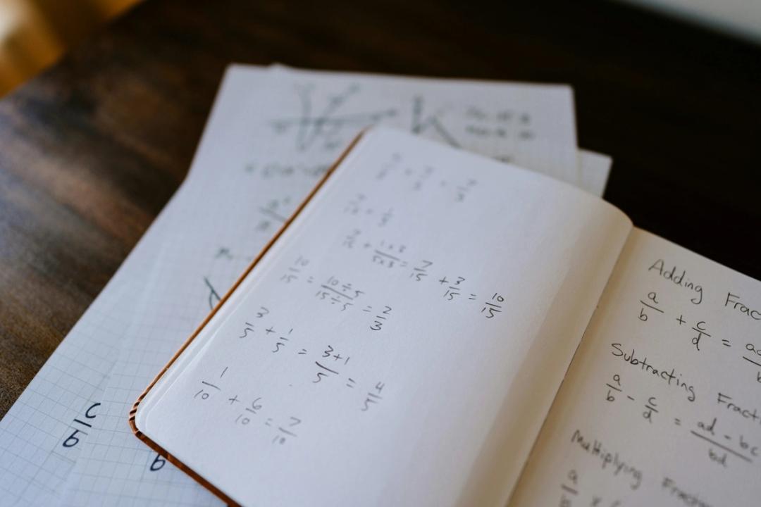 Åpen mattebok med brøkregning og ligninger, sammen med ruteark - slik vil du jobbe med praktisk matematikk i 2P.
