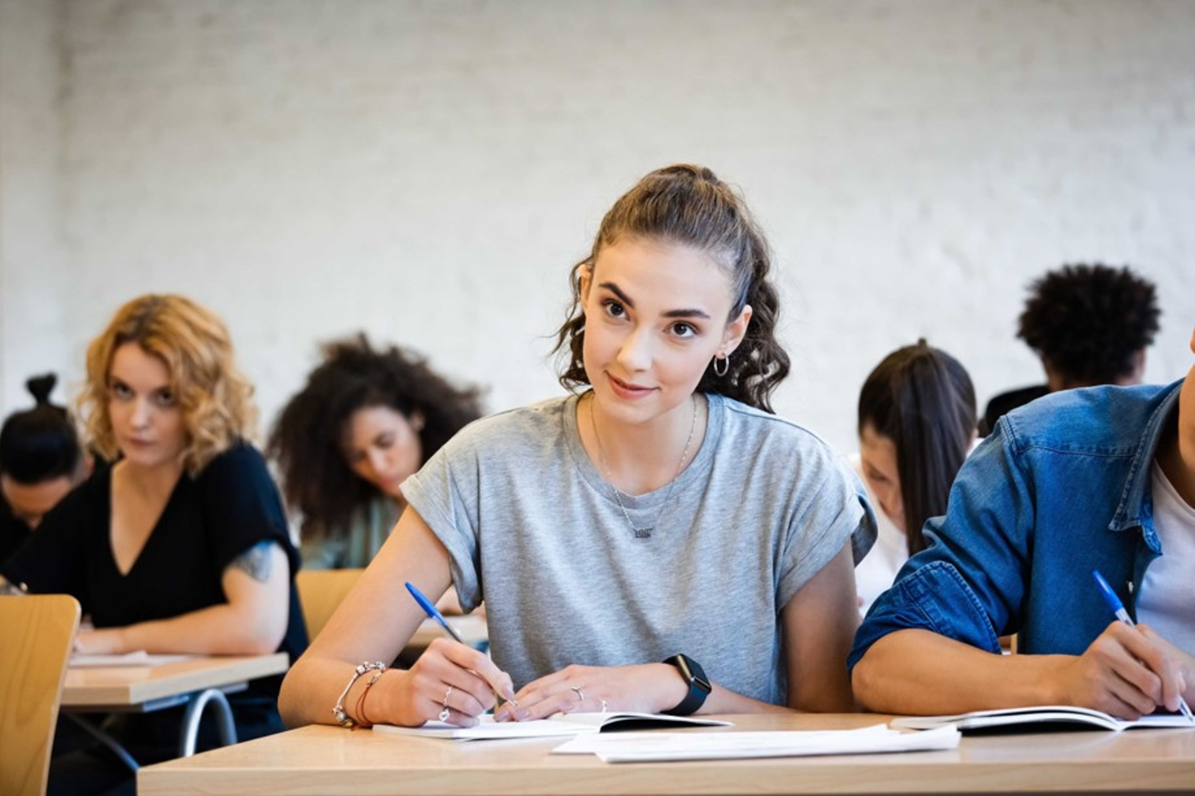 Ung kvinne sitter i et klasserom og skriver i en notatbok. 