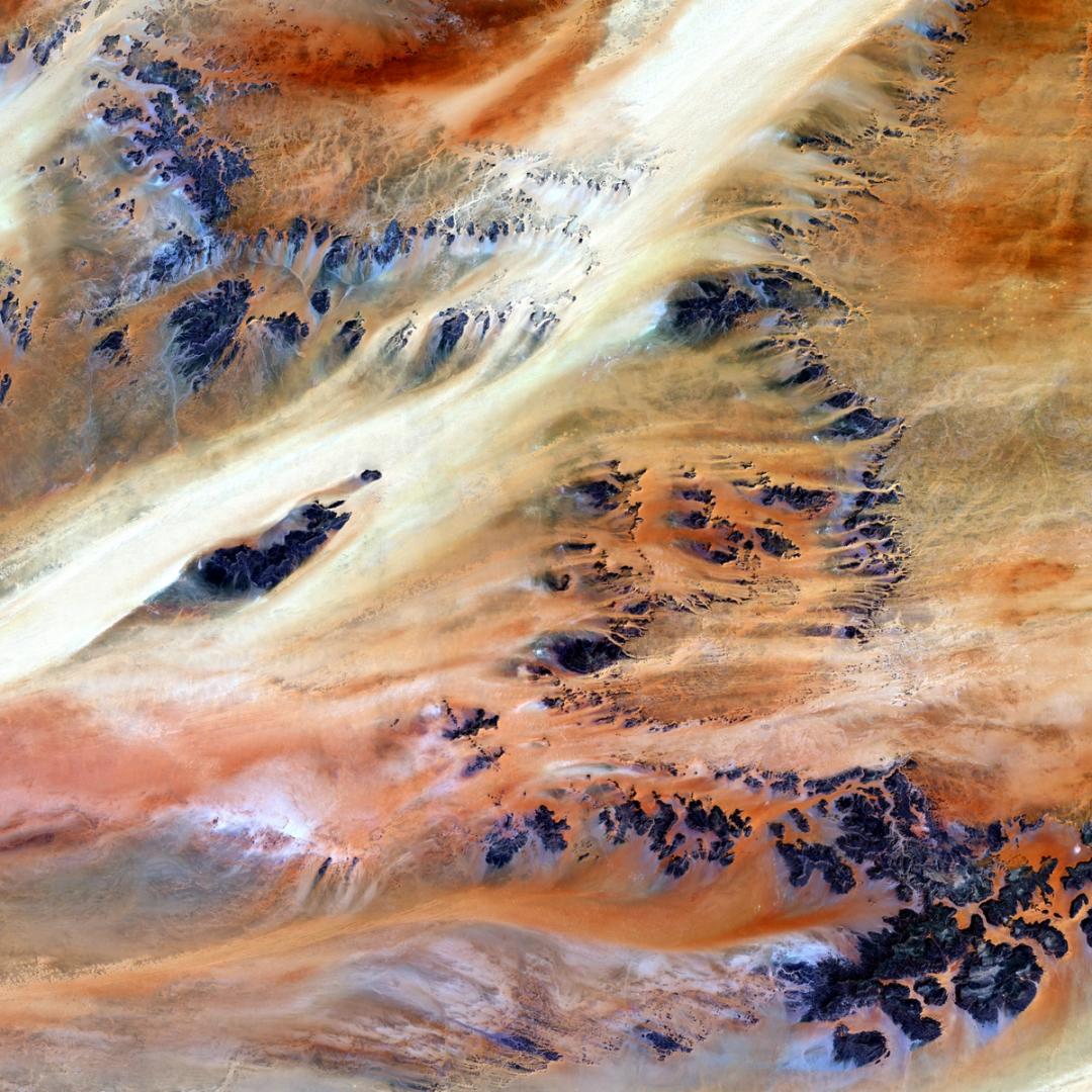 Satellittbilde av fargerike ørken- og fjellformasjoner, illustrerer jordas geologiske prosesser.