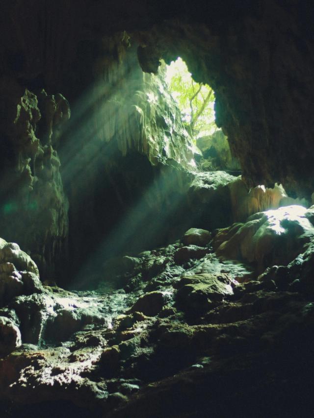 Bilde av sollys som strømmer inn i en mørk fjellhule og lyser opp steinene.