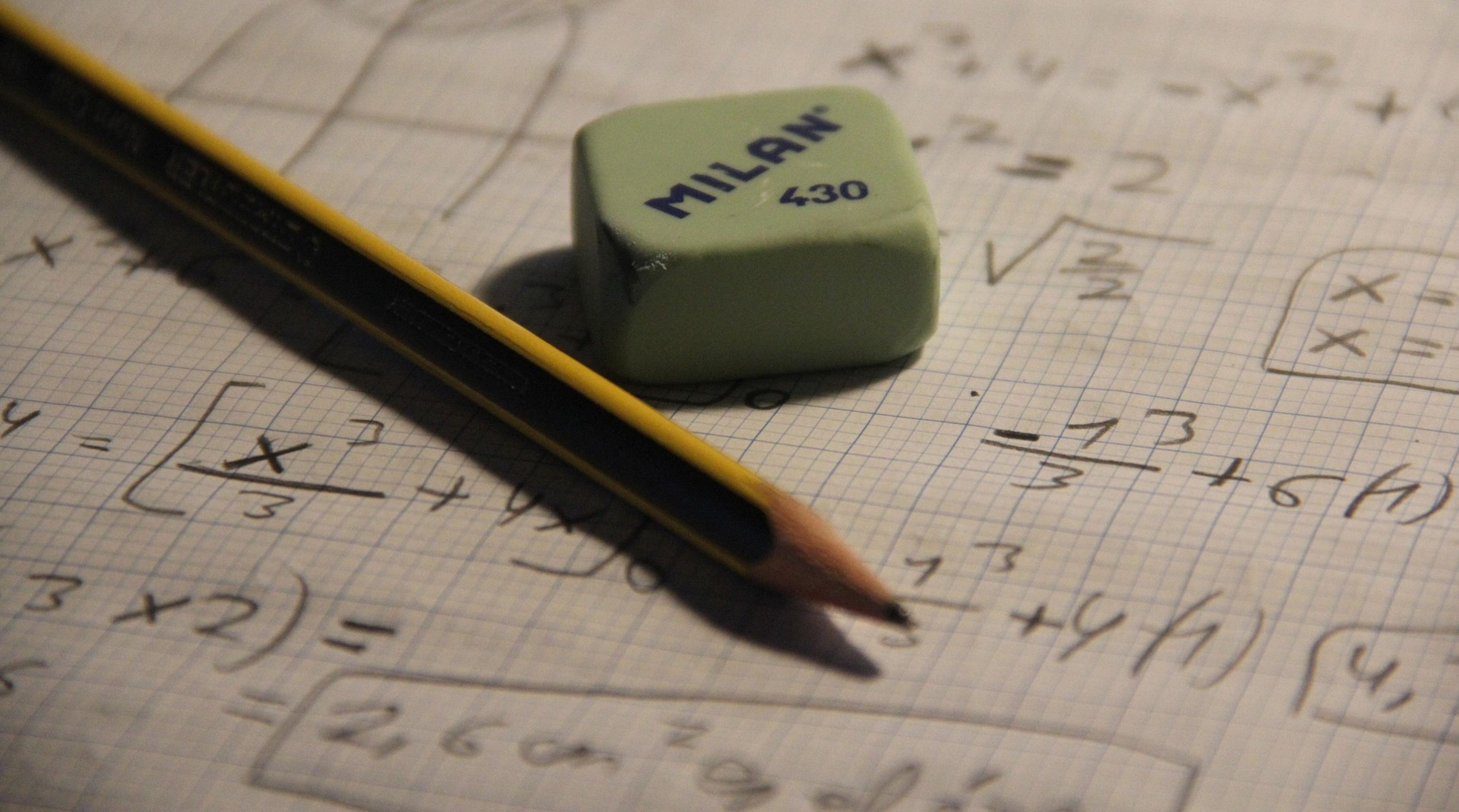 En blyant og et viskelær ligger oppå et ruteark med diverse utregninger på.