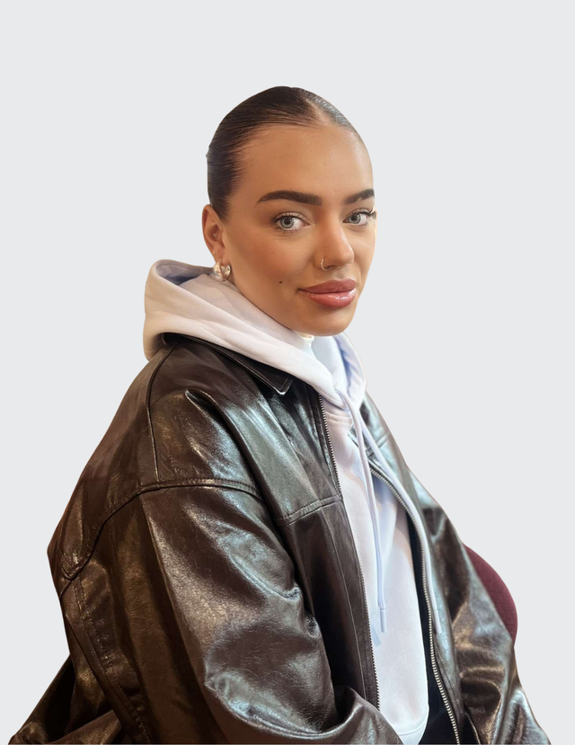 Smilende ung kvinne i lys genser og brun jakke.