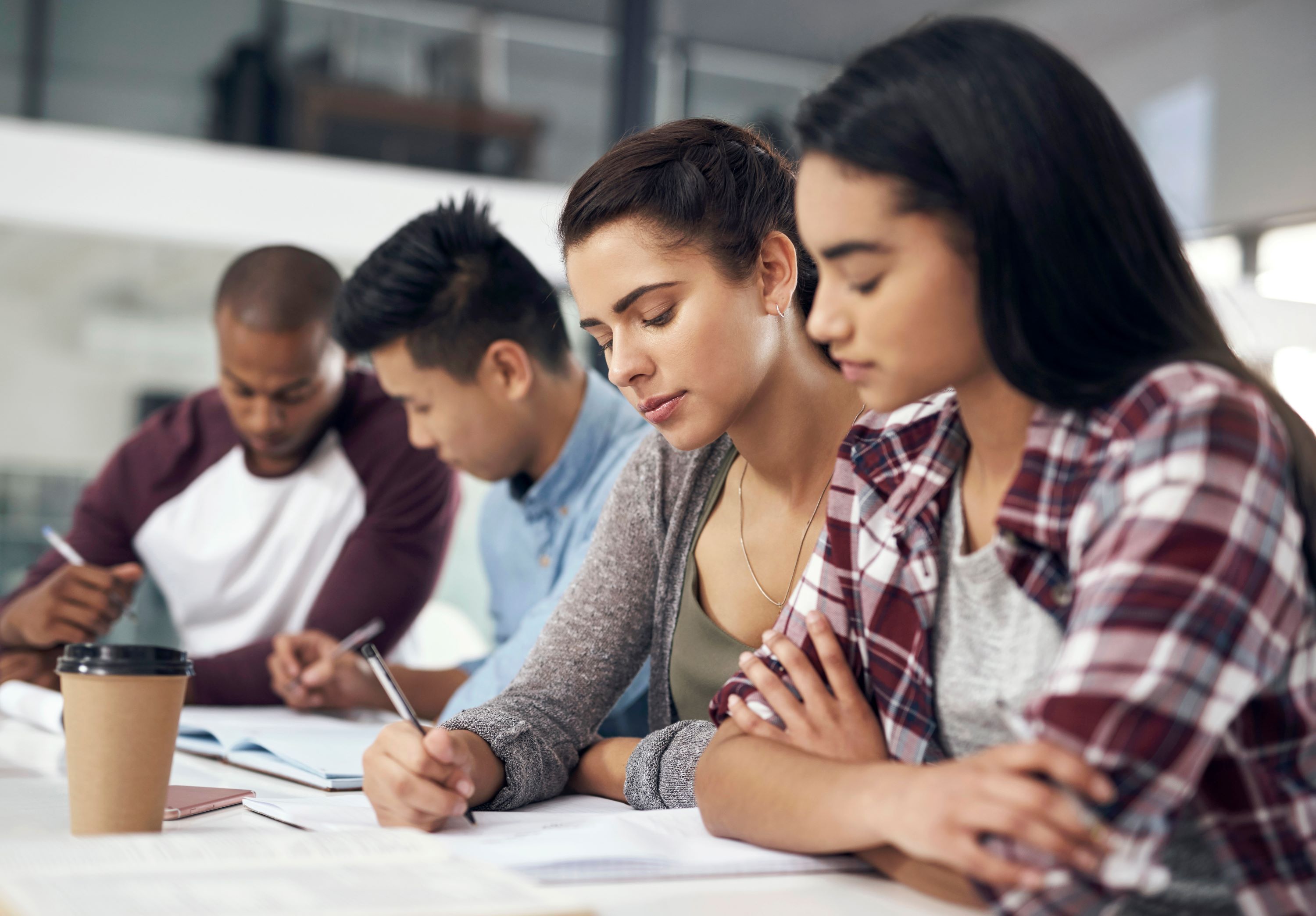 Studenter sitter ved et bord og jobber med notater og lærebøker i et lyst klasserom.