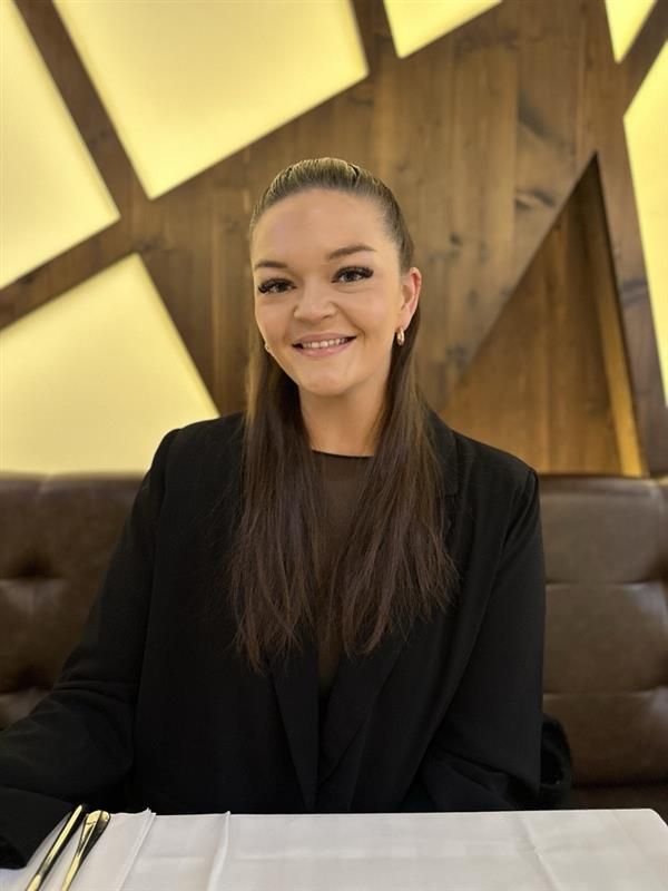 Avdelingsleder i Sonans Stavanger, Marie Welo Hansen, smiler ved et bord med en trevegg i bakgrunnen.