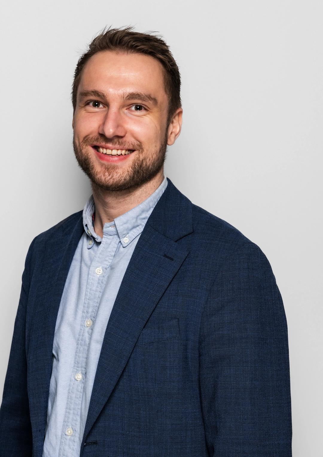 Avdelingsleder for Sonans Kristiansand, Herman Holmeide Halvorsen, smiler med lys bakgrunn