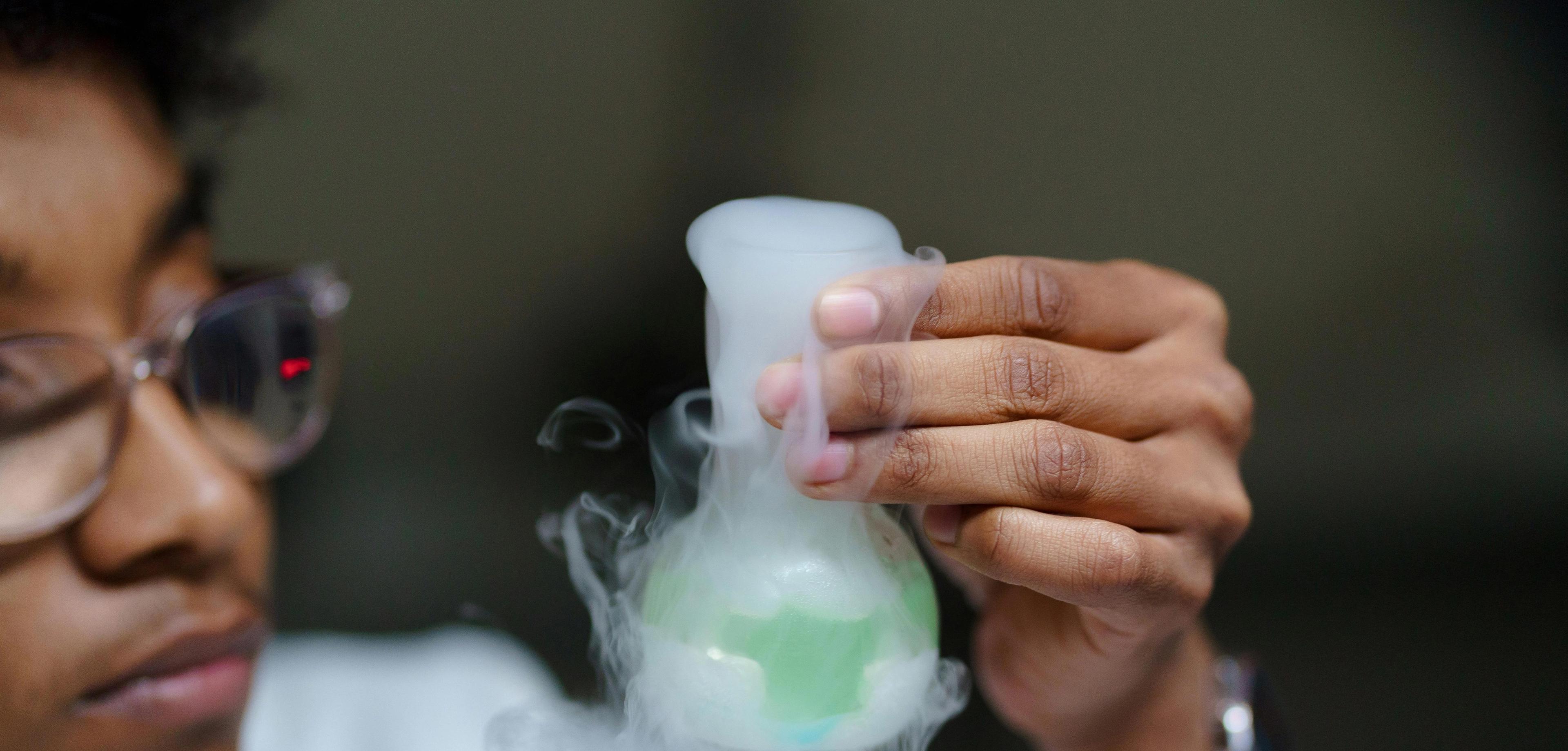 Student som studerer en kjemisk reaksjon i et glass med grønn væske og røyk.