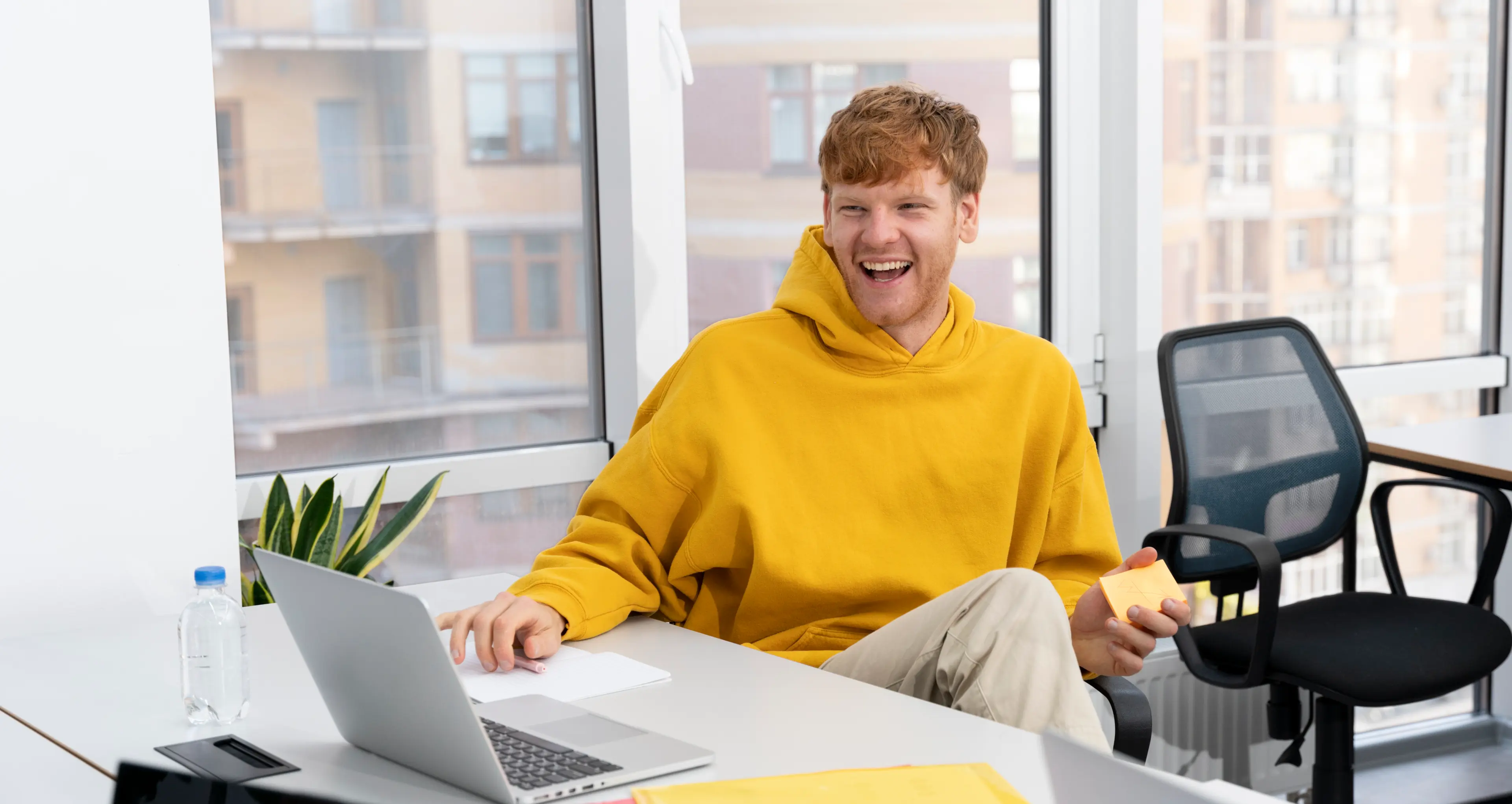 En smilende ung mann i gul hettegenser jobber på en laptop.