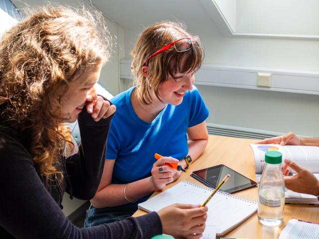 Studenter samarbeider om eksamensforberedelser ved et bord, med notater, bøker og nettbrett.