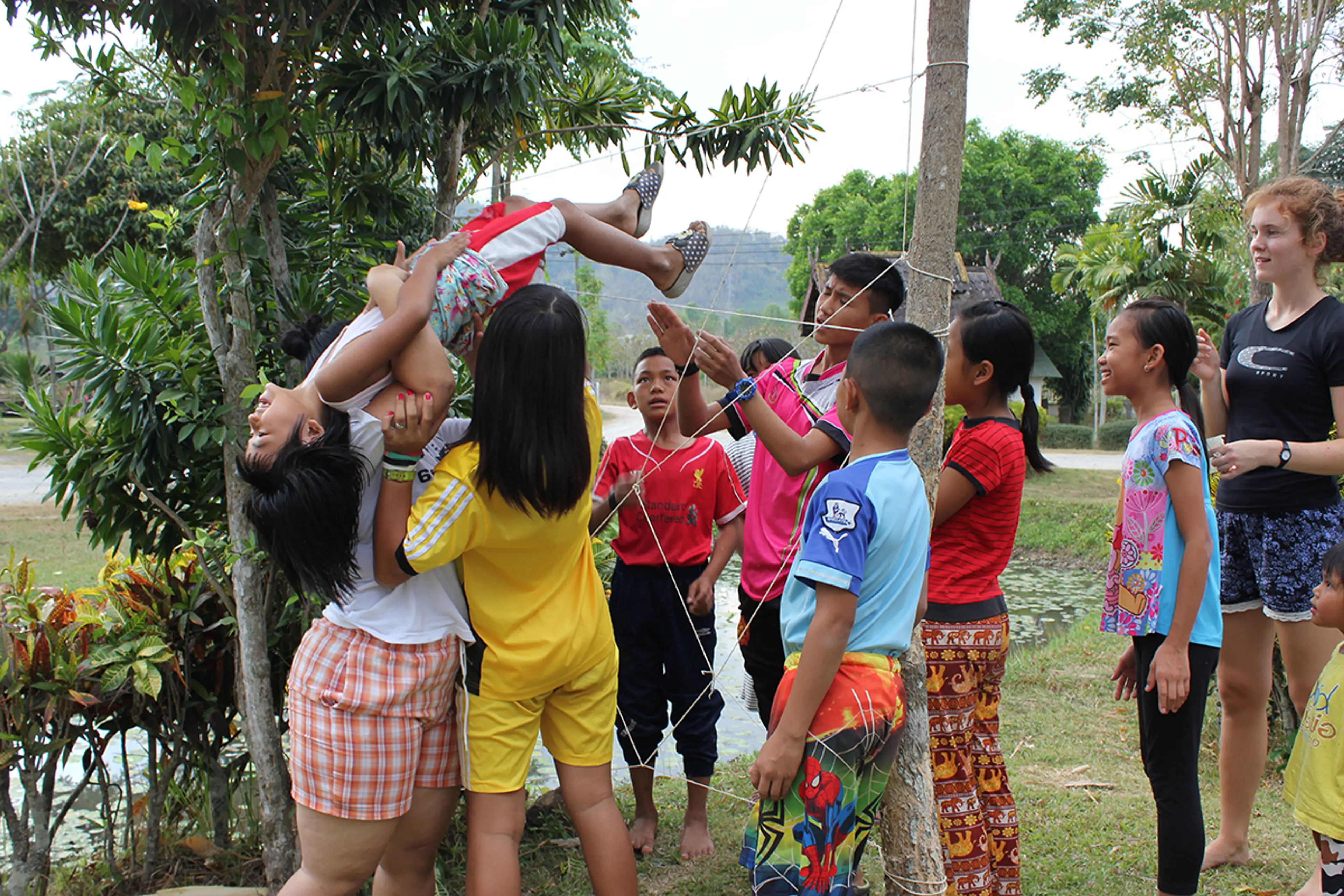Barn i Baan Chivit Mai samarbeider om en utendørs gruppelek med et nett, mens en voksen veileder dem.