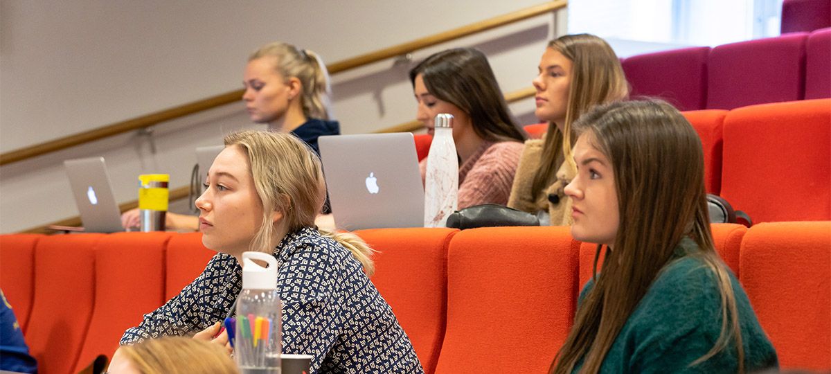 Sonans studenter følger med i undervisning i en forelesningssal, med notater, vannflasker og bærbare datamaskiner.