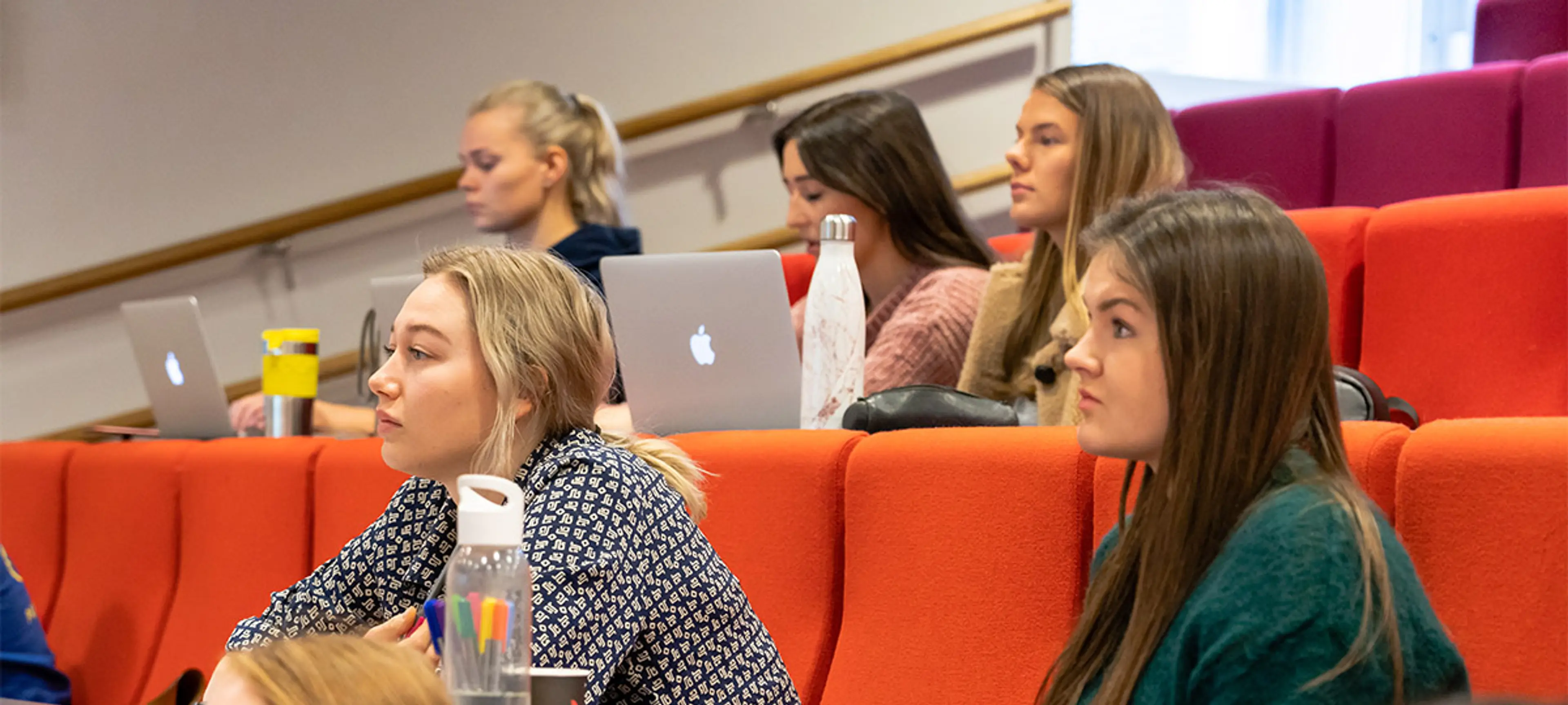 Sonans studenter følger med i undervisning i en forelesningssal, med notater, vannflasker og bærbare datamaskiner.