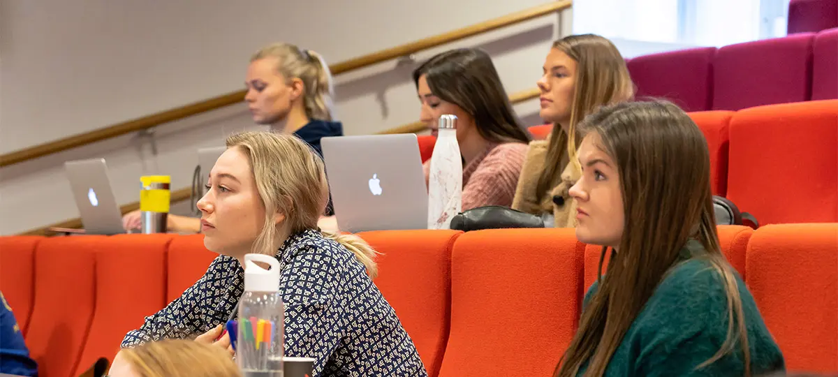 Sonans studenter følger med i undervisning i en forelesningssal, med notater, vannflasker og bærbare datamaskiner.