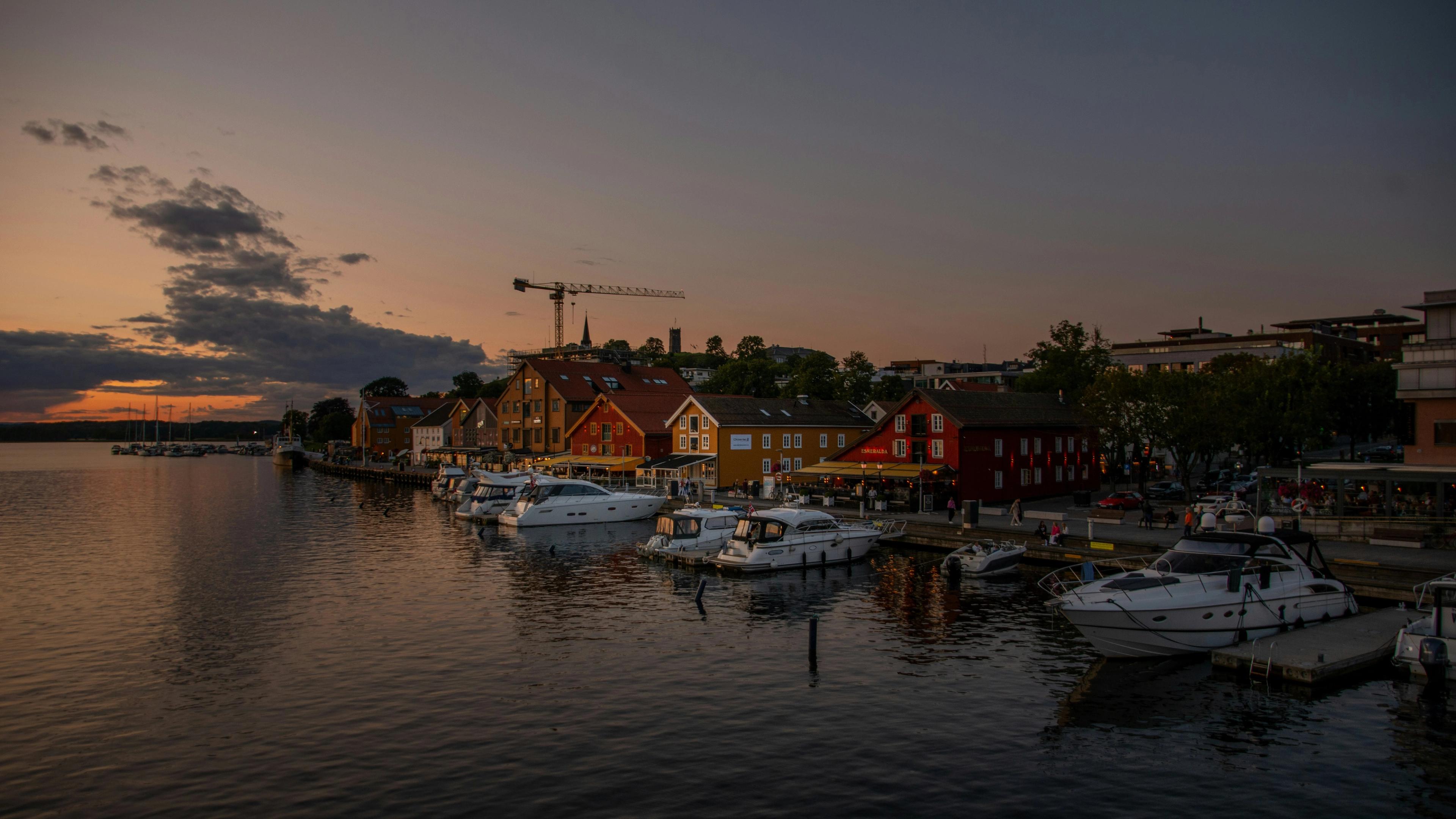Brygga i Tønsberg i solnedgang, med båter og fargerike trehus langs vannet.