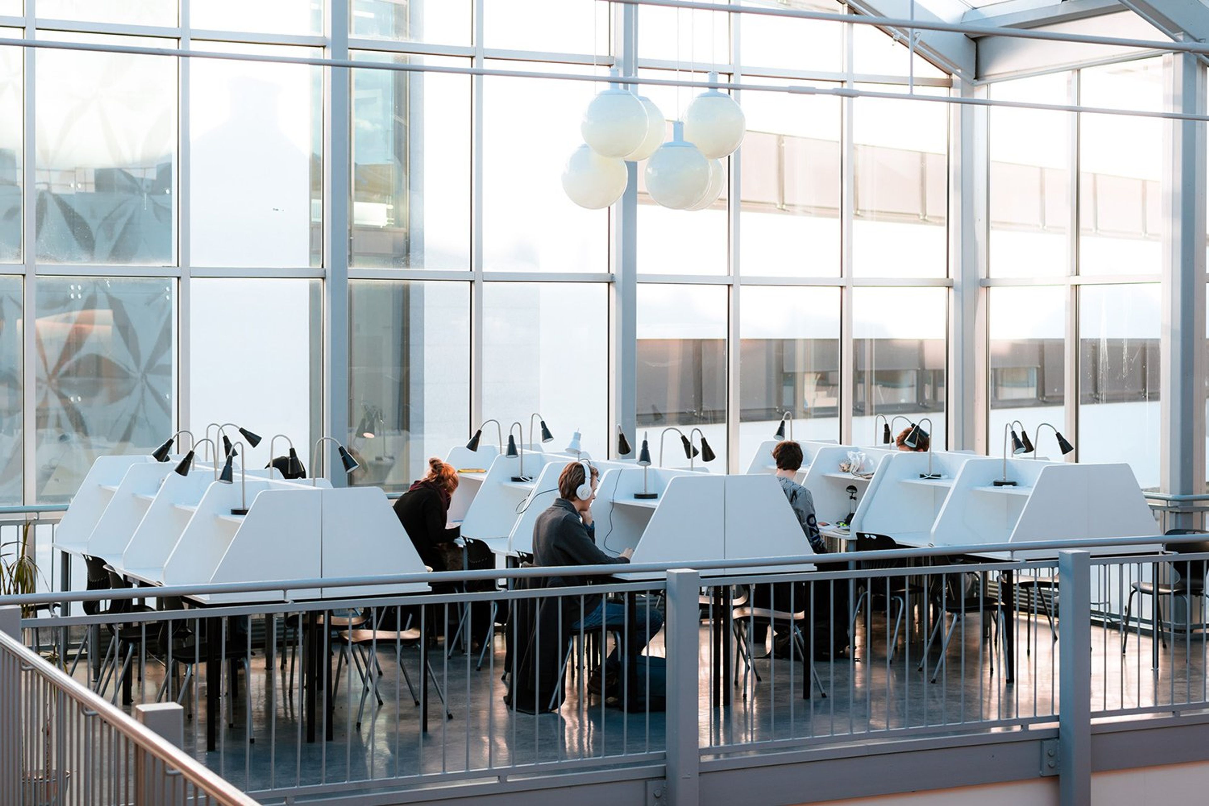 Studenter sitter og jobber i lyse og moderne lesesaler hos Sonans Oslo, med store vinduer og individuelle arbeidsplasser.