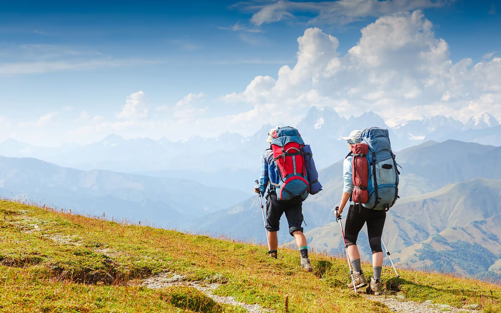 Zwei Wanderer mit Rucksack auf einem Almweg über dem Tal
