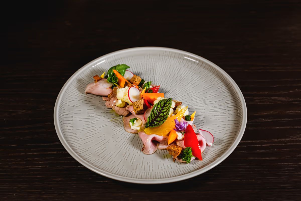 Bunt angerichteter Teller mit Speck, Gemüse und Kräutern