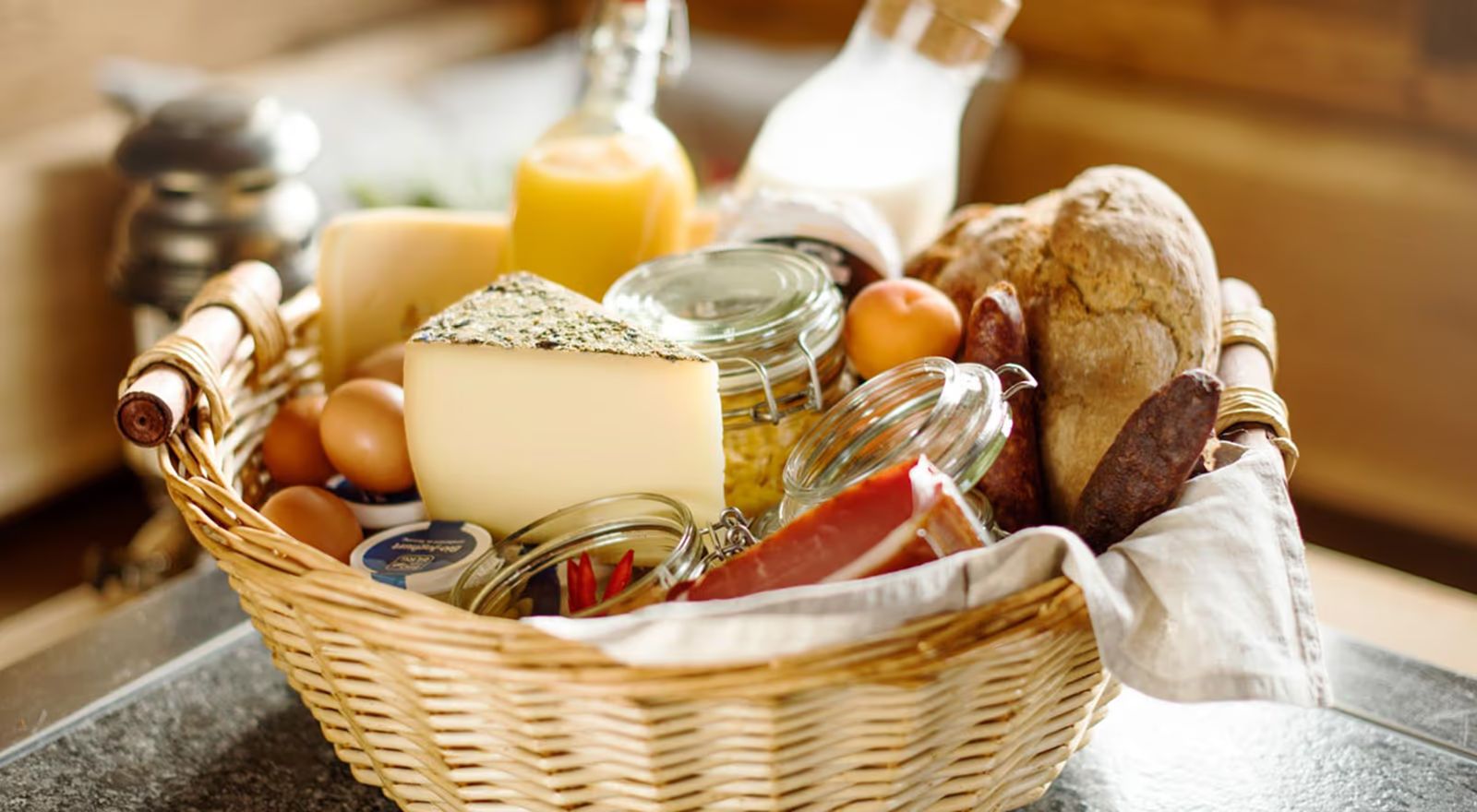 Frühstückskorb mit Brot, Käse, Eiern, Marmelade und Saft